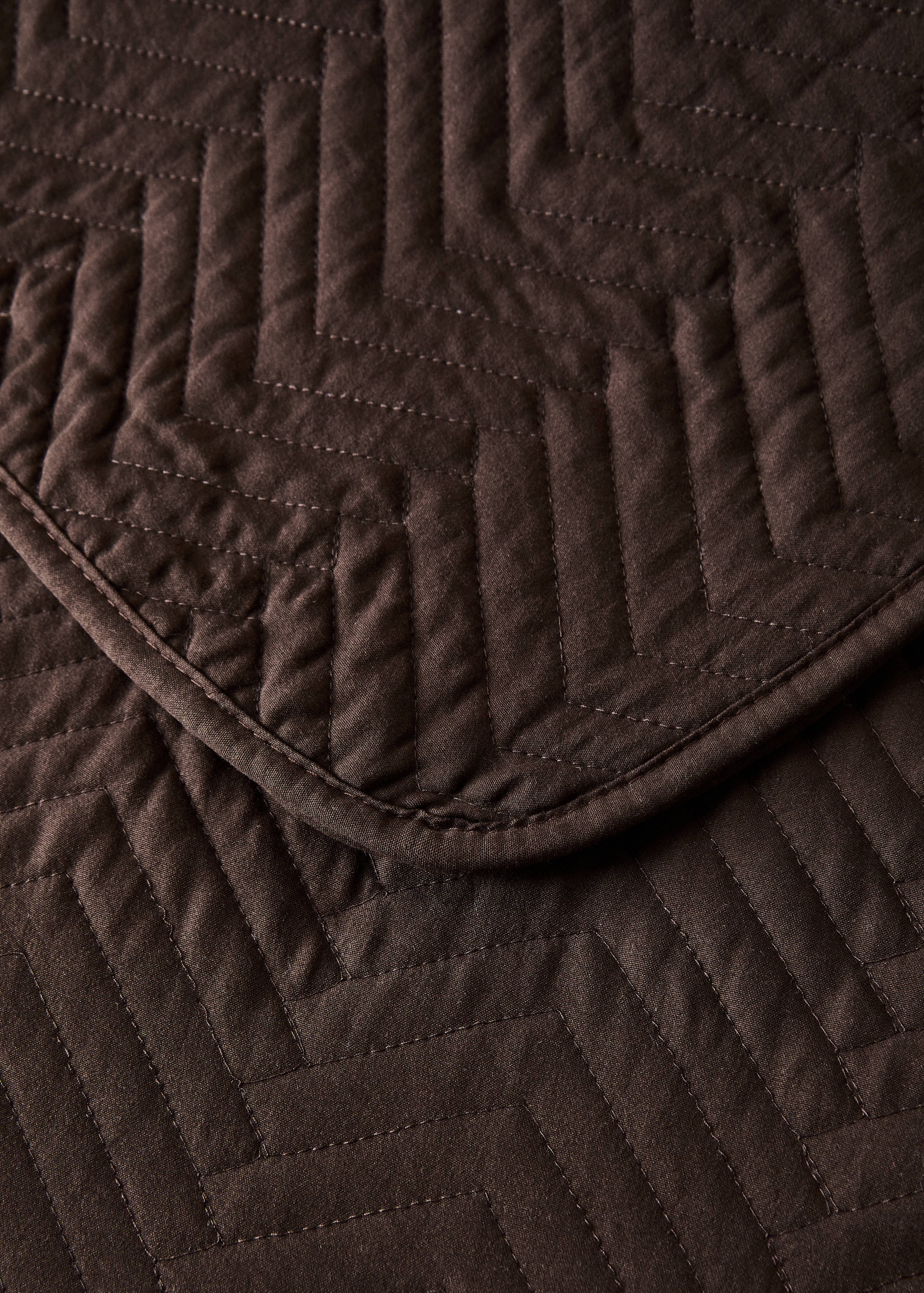 Brown quilted bedspread detail with chevron pattern.