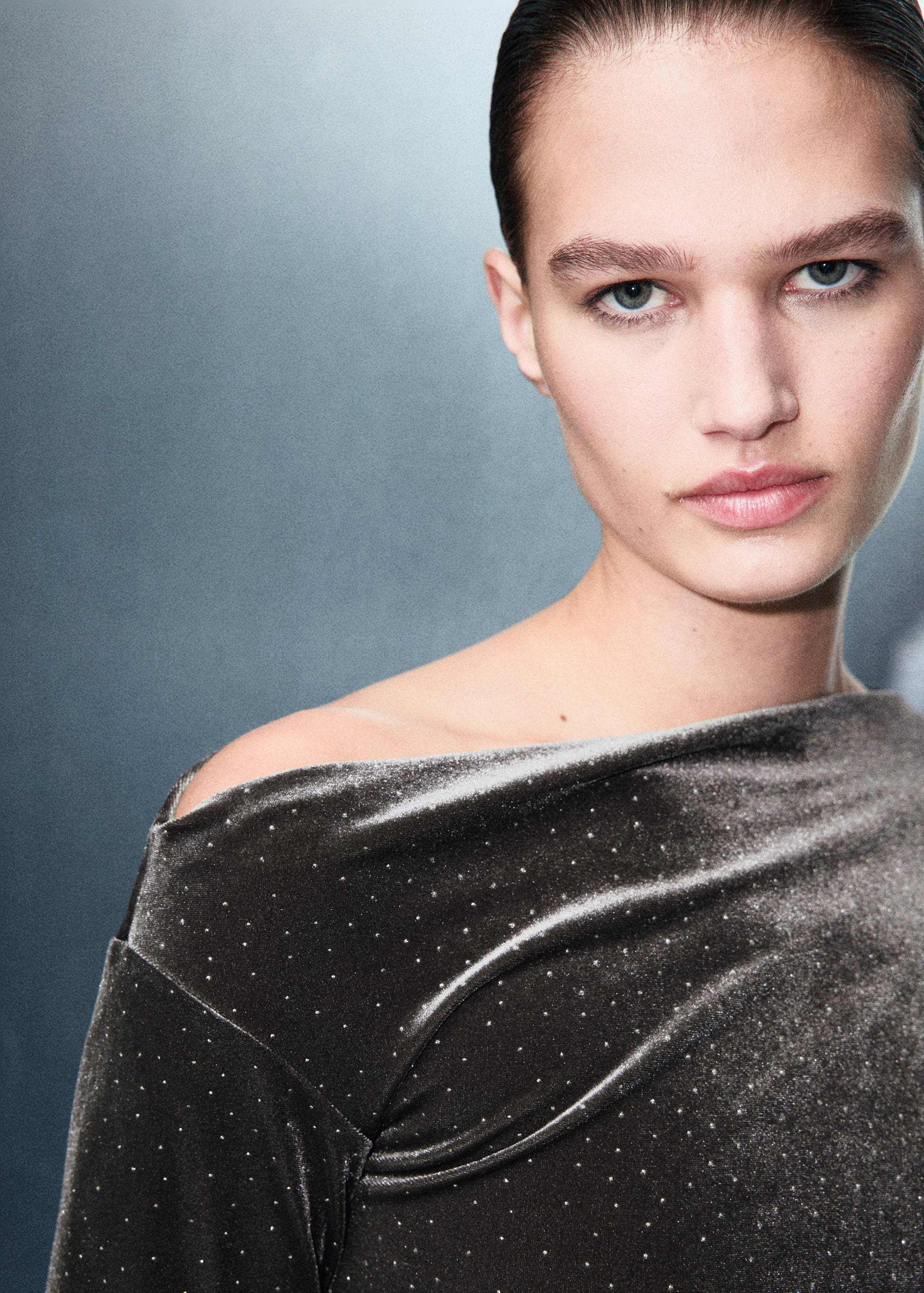 Close-up of a grey velvet dress with metallic studs and an asymmetrical neckline.