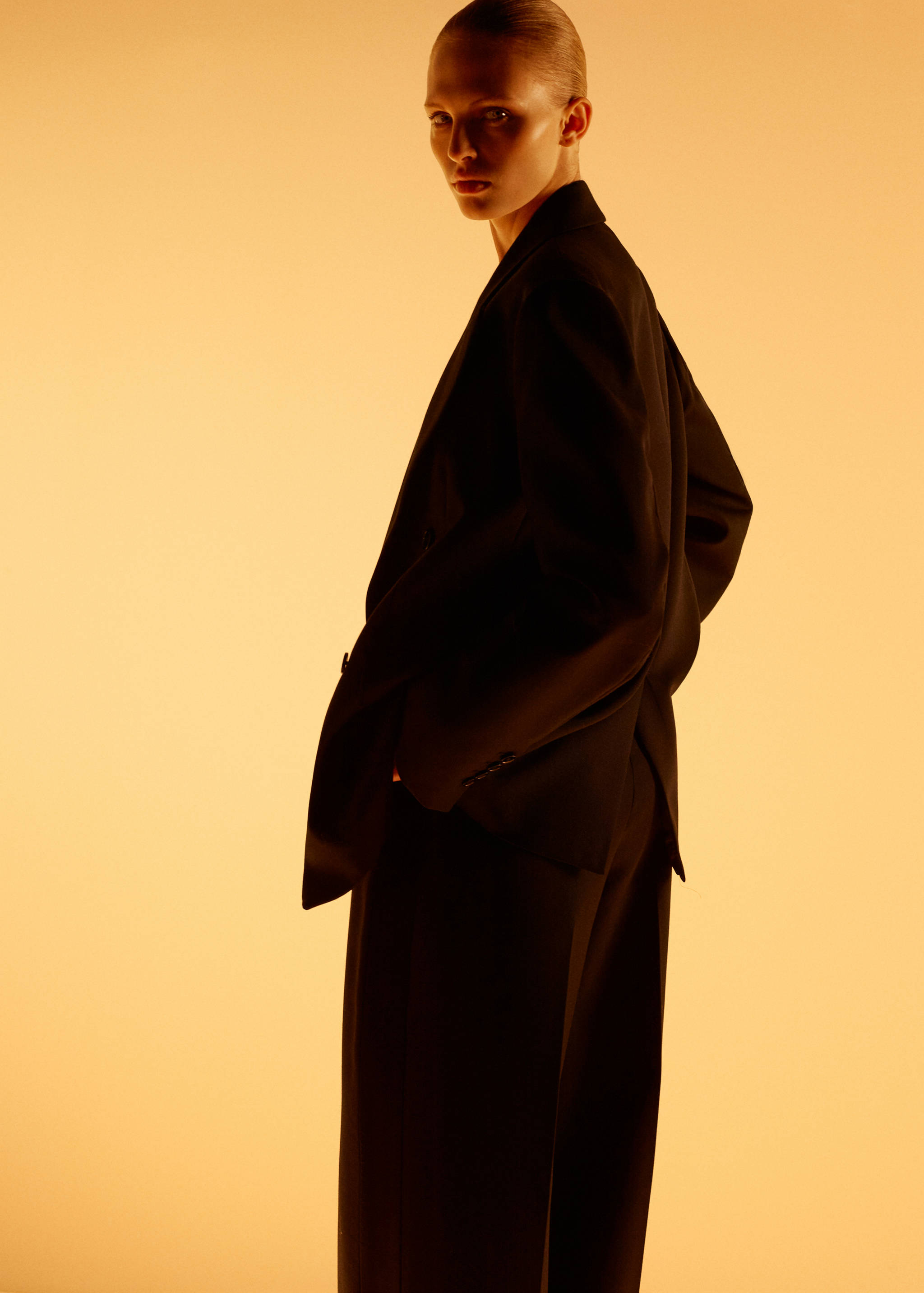 Black trousers worn with a matching blazer against a warm lit background.