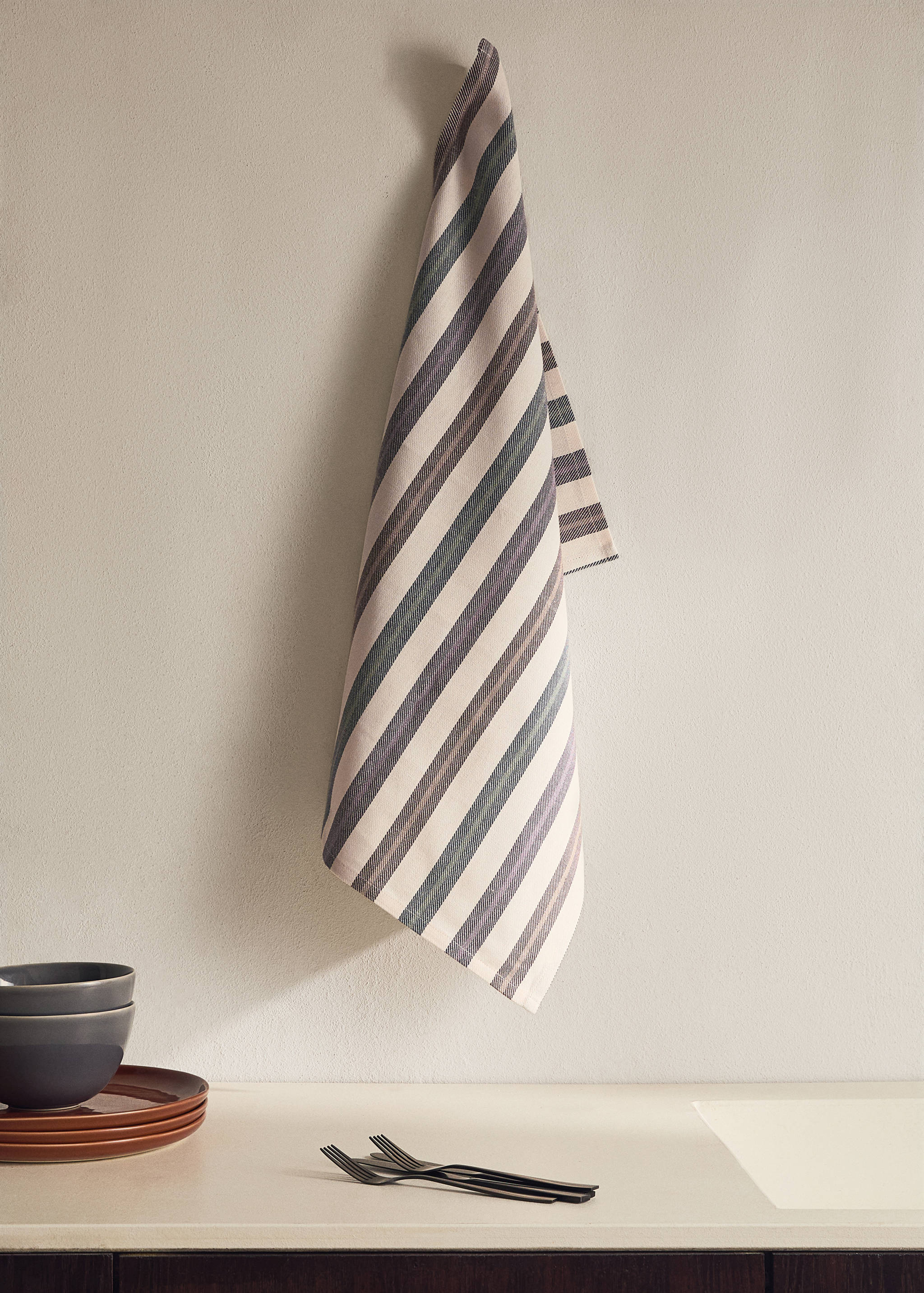 Striped kitchen towel hanging against a plain wall above a countertop.