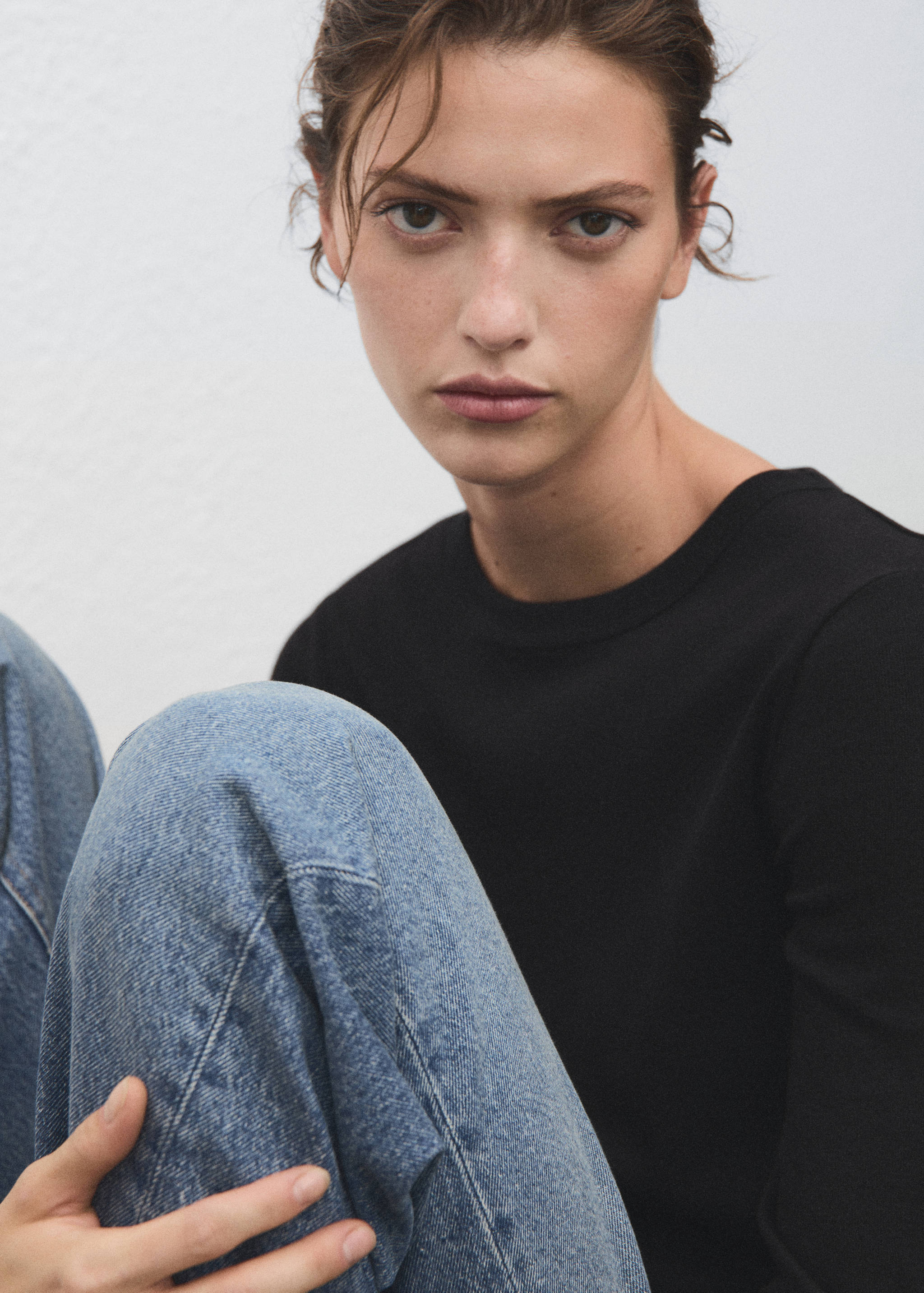 Black t-shirt with a round neckline worn with blue denim trousers.