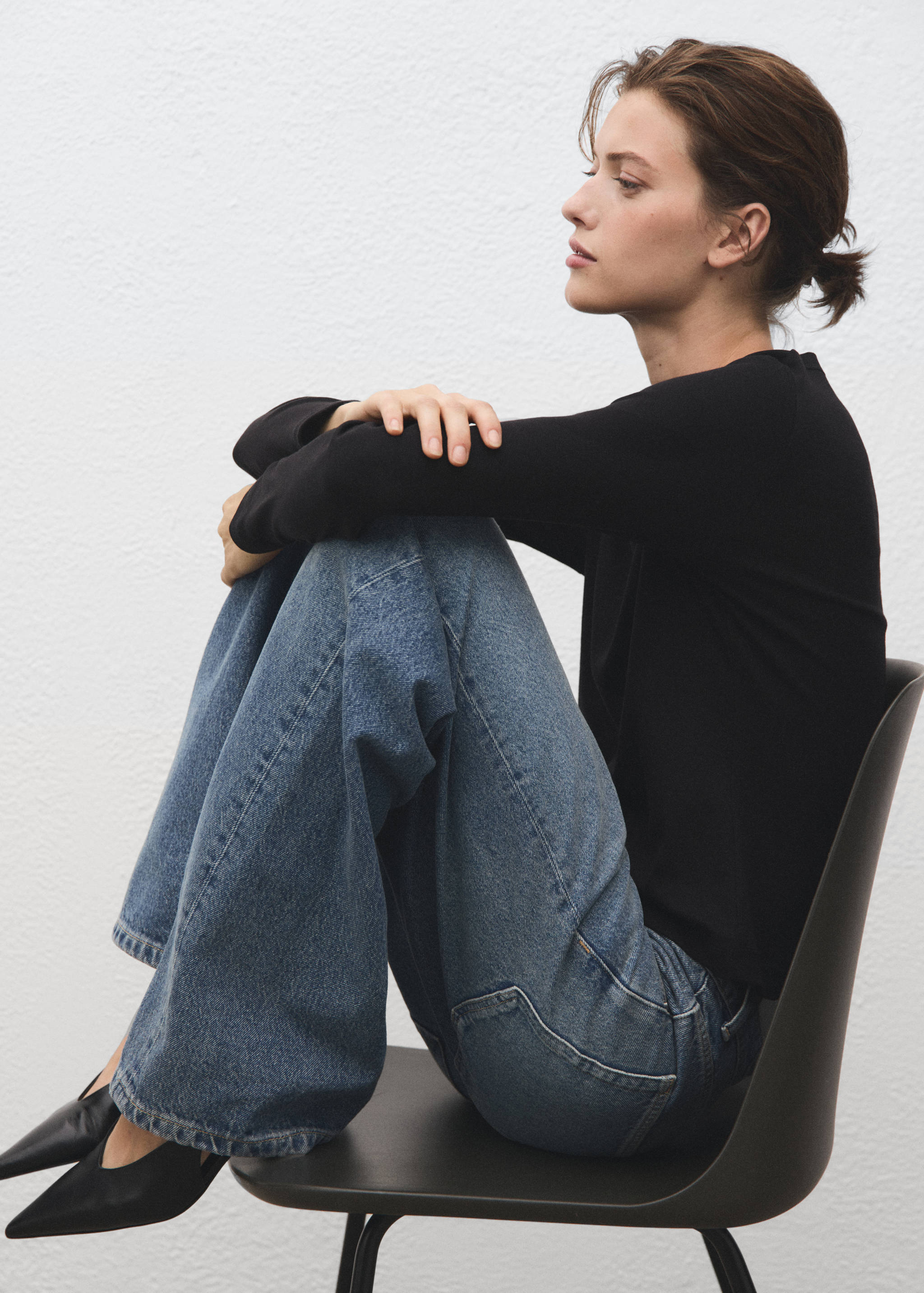 Black long-sleeved t-shirt with a round neckline, worn with blue denim trousers.