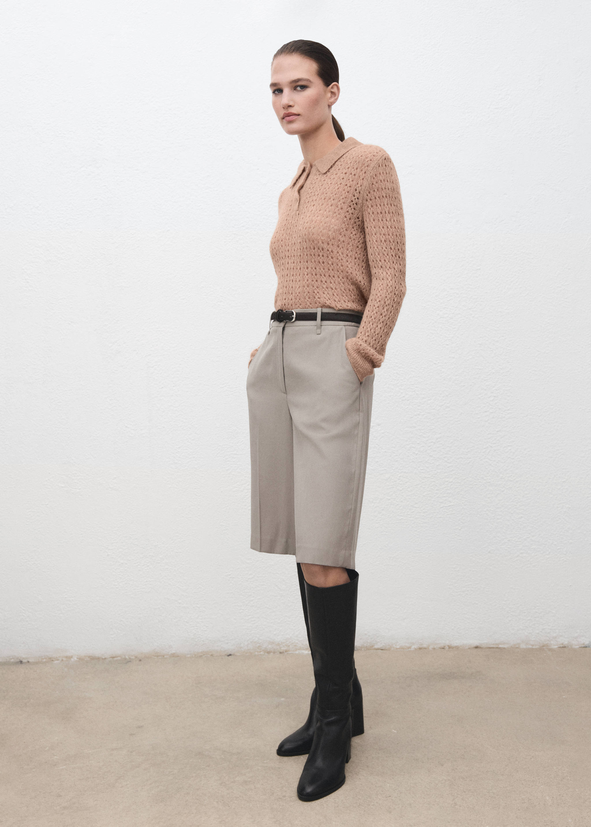 Camel-brown open-knit polo shirt worn with grey Bermuda shorts and black knee-high boots.