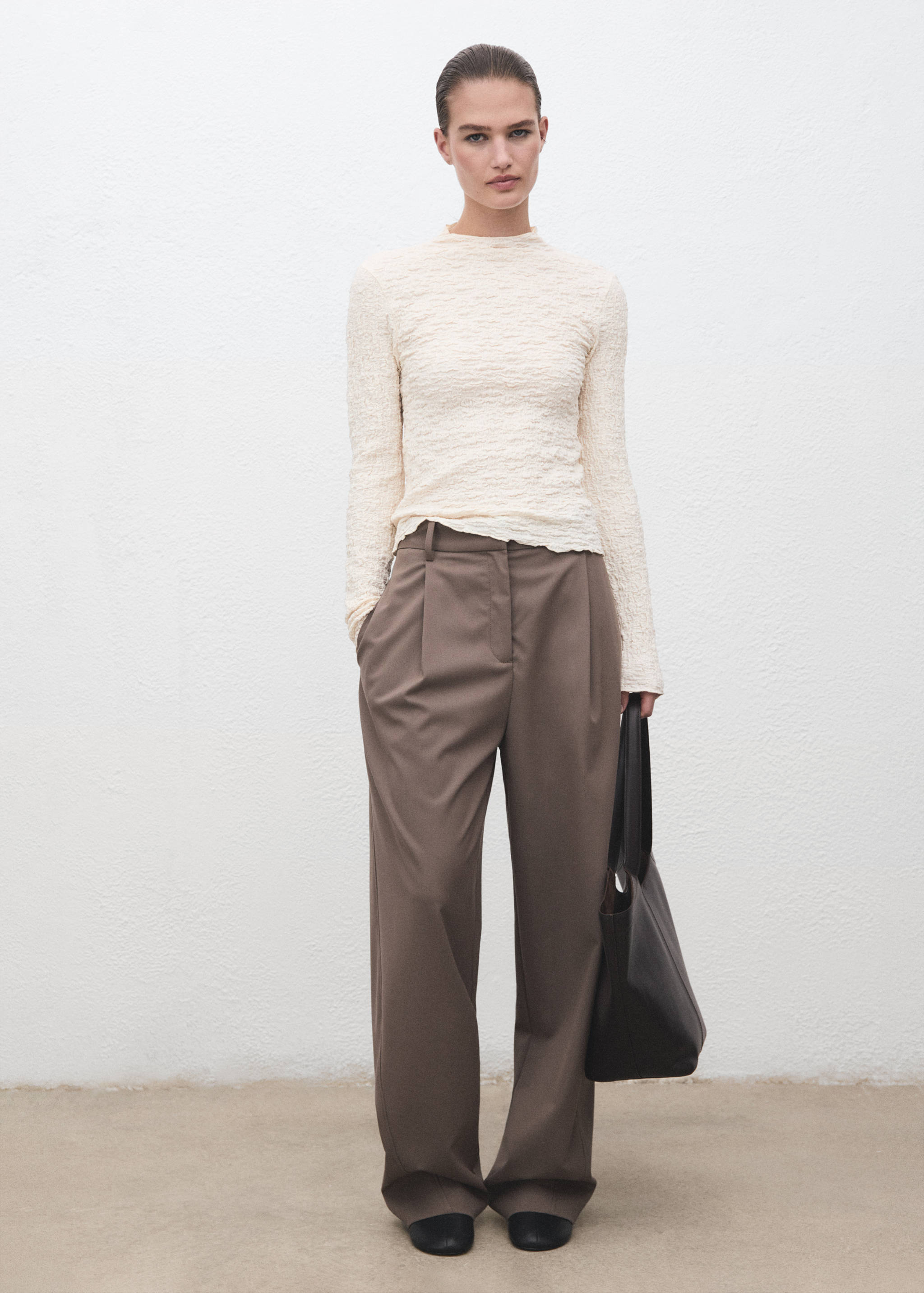 Ecru textured long-sleeve top with a high neckline worn with brown trousers.