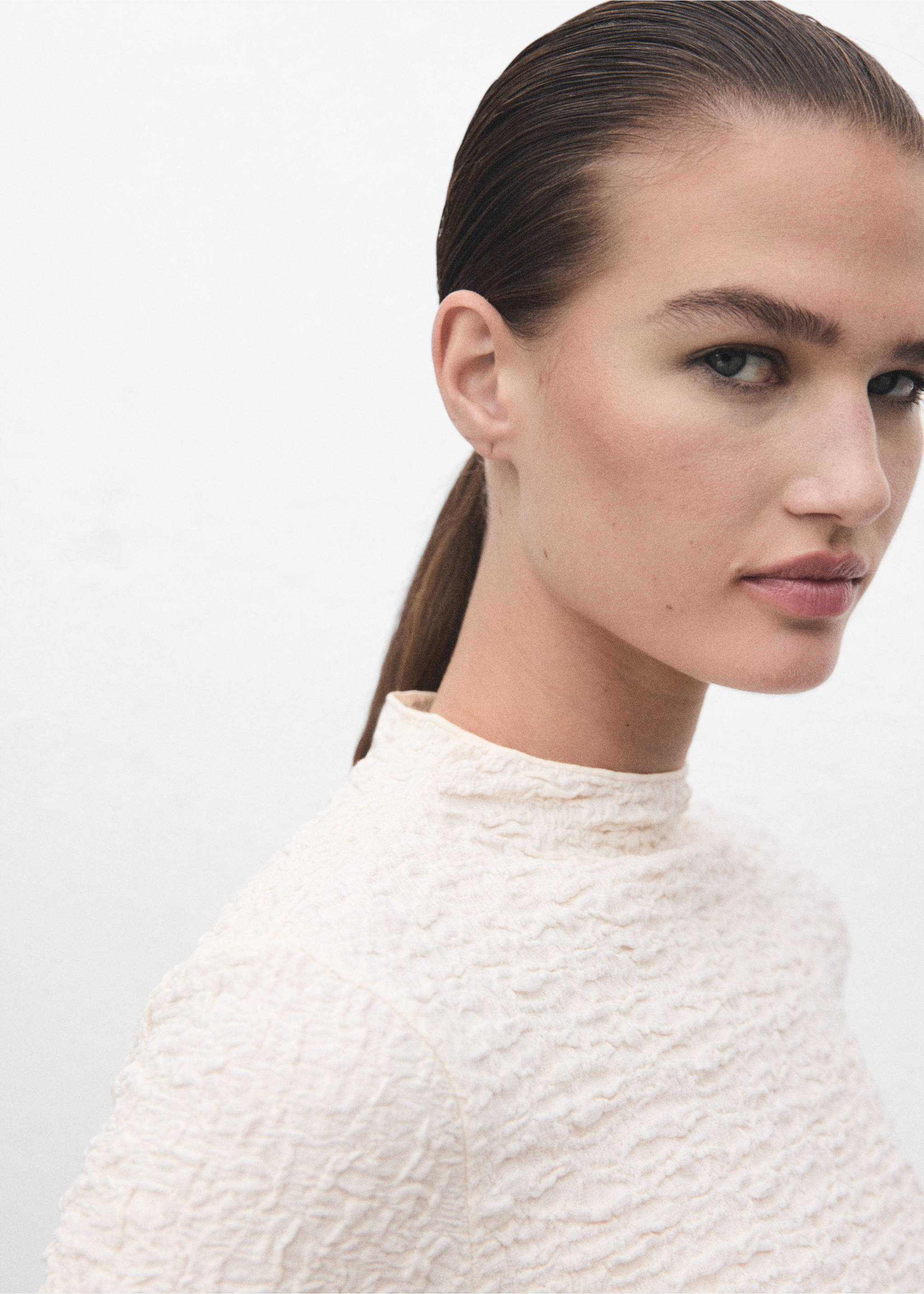 Close-up of a model wearing a cream textured high-neck top., Ecru. Ref: 17057793-00.