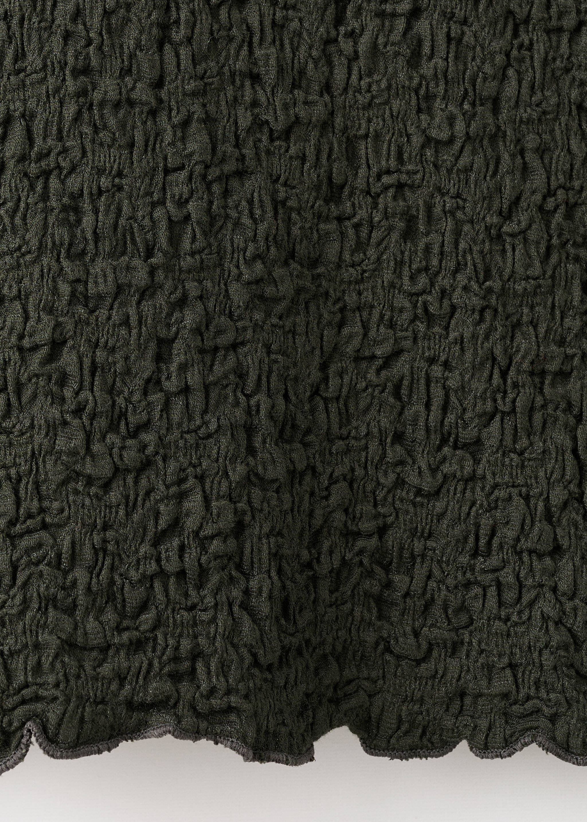 Close-up of a dark green textured top with a puckered finish and lettuce hem.