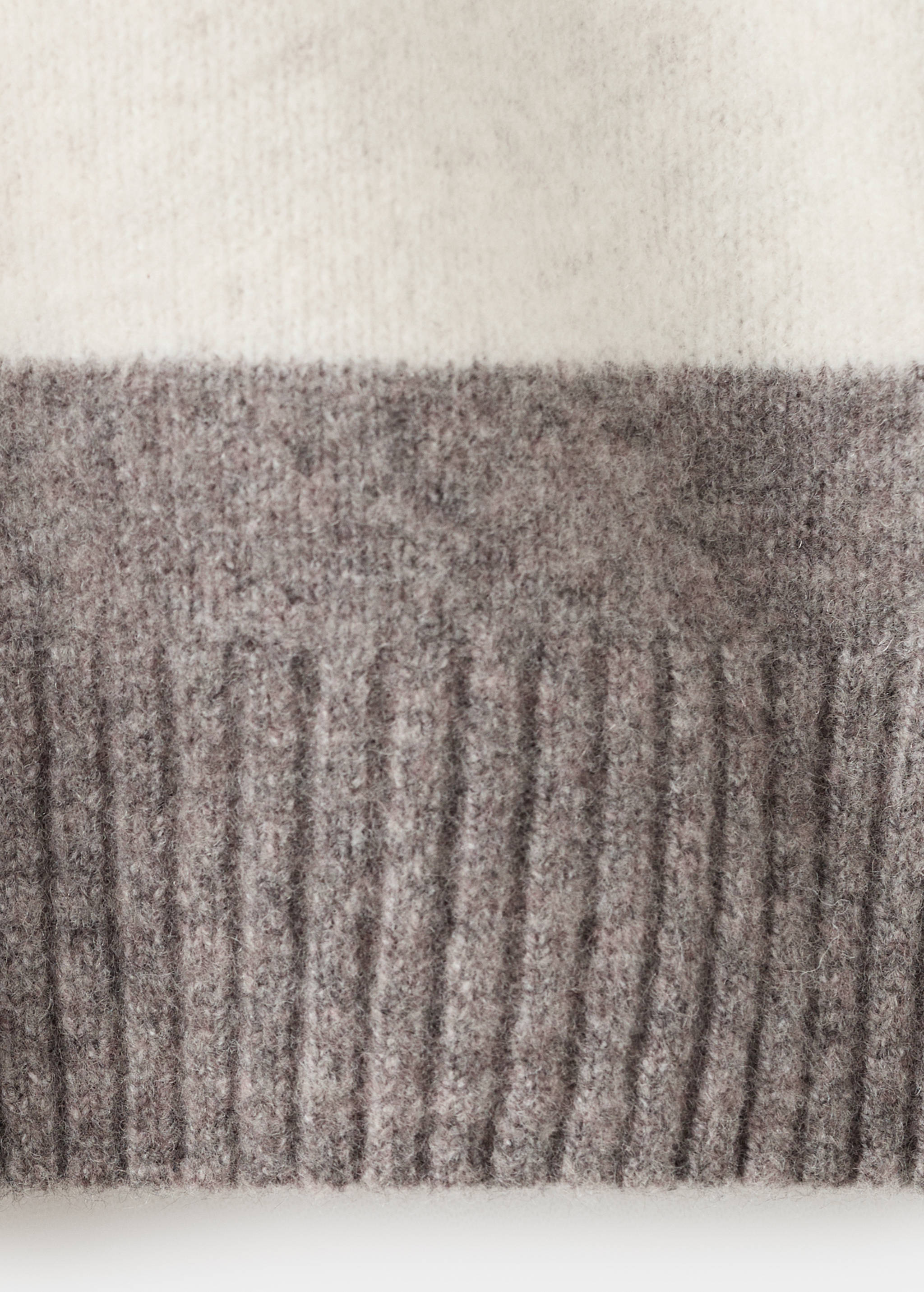 Close-up of a men's knit jumper with an off-white and dark brown colour-block design and ribbed hem.