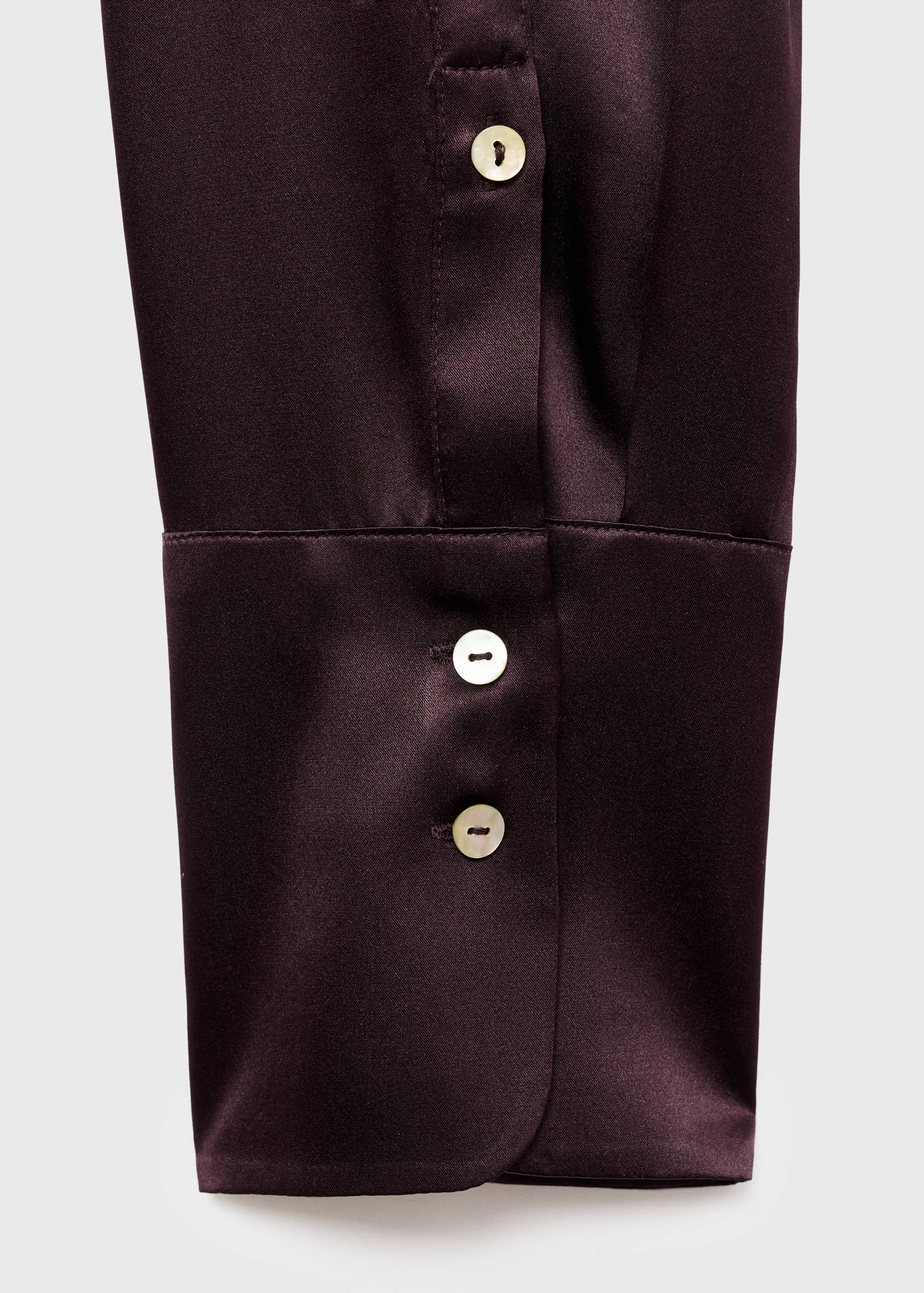 Close-up of a dark plum satin shirt cuff with two pearlescent buttons.