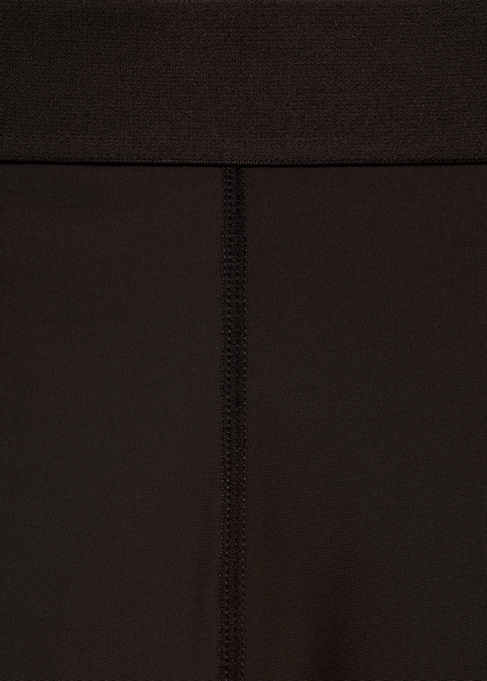 Close-up of dark brown leggings showing the elasticated waistband and central seam.