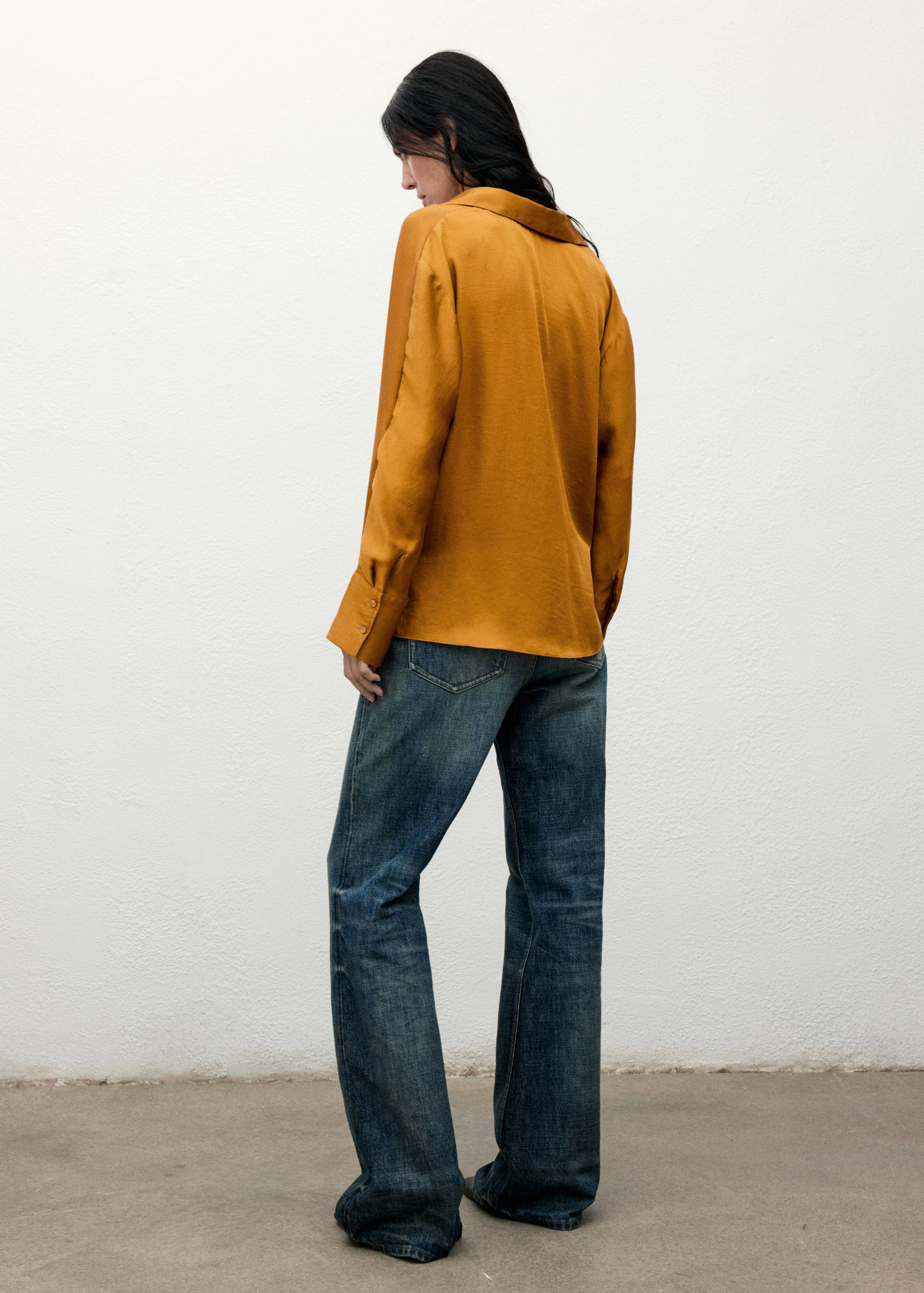 Amber gold shirt with long sleeves seen from the back, worn with blue trousers.