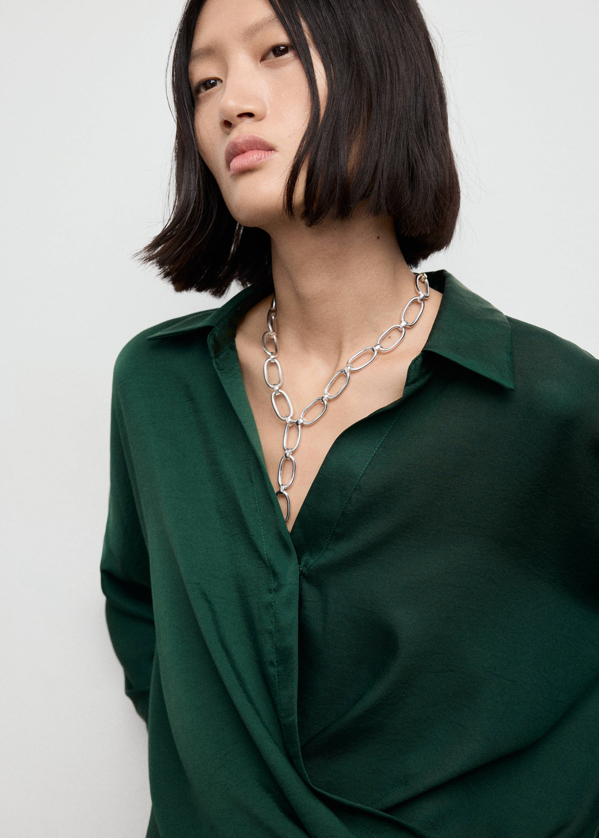 Dark green shirt with a classic collar and V-neckline, worn with a silver chain necklace.