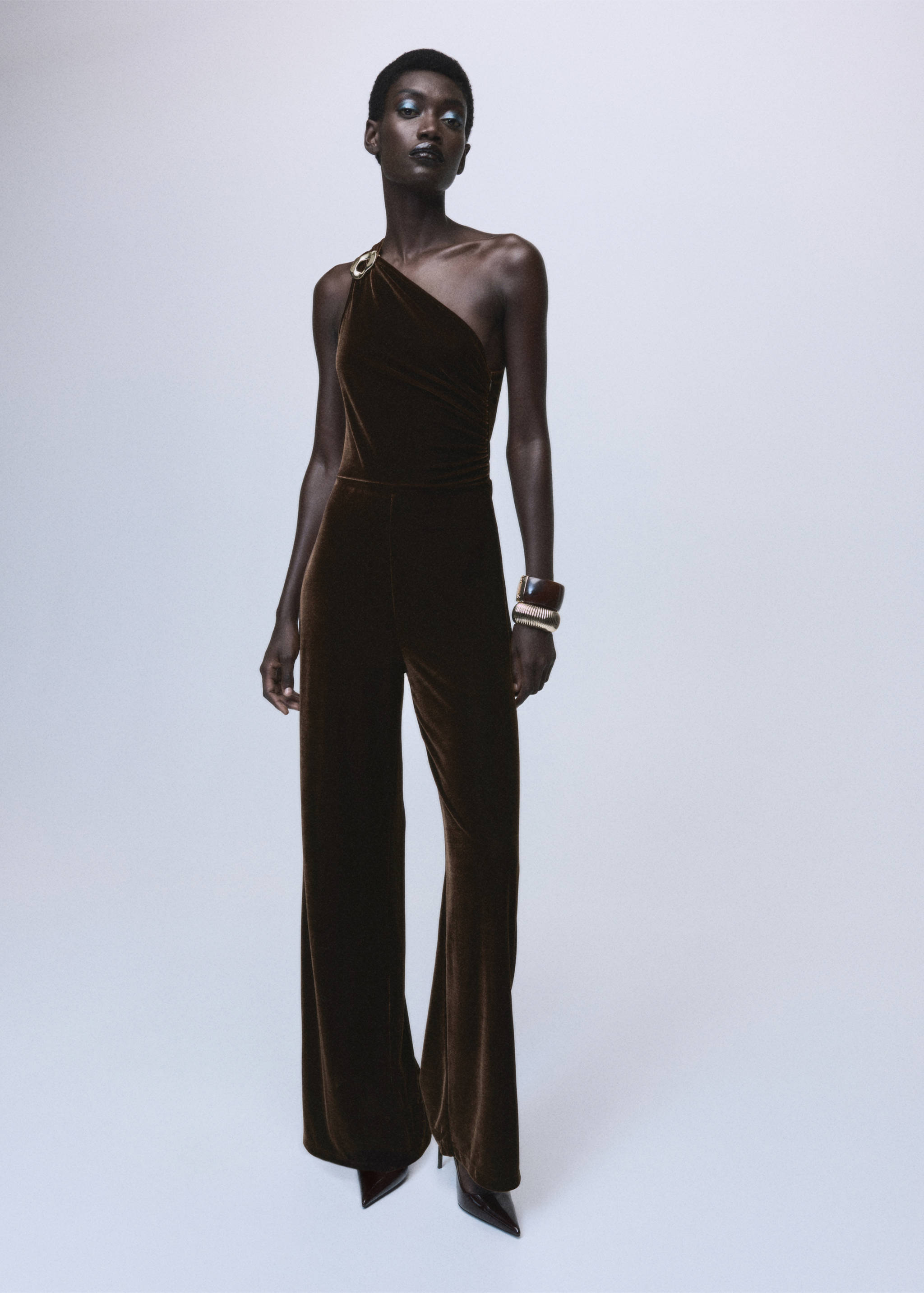 Dark brown velvet one-shoulder jumpsuit with wide-leg trousers.