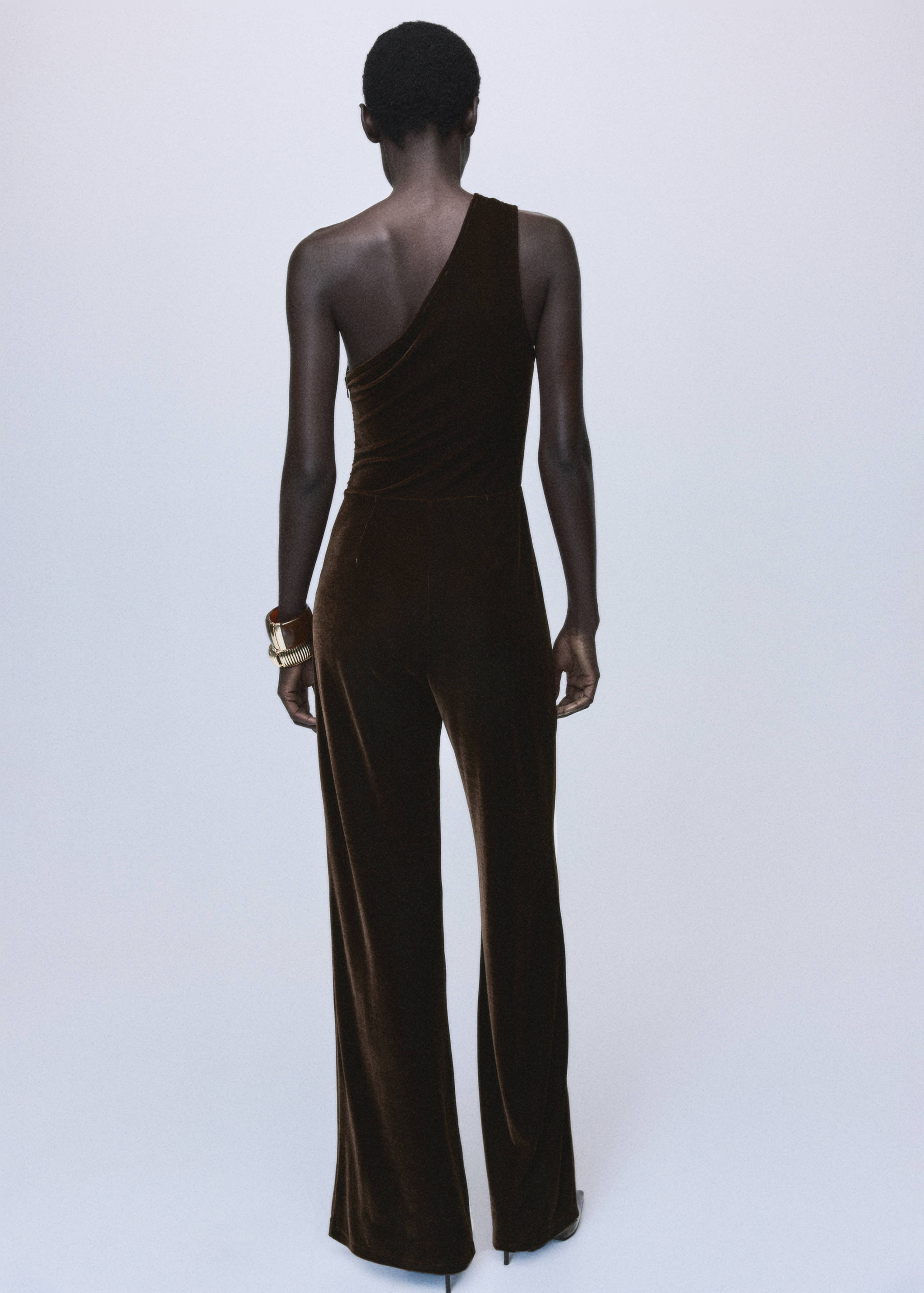Back view of a dark brown velvet one-shoulder jumpsuit.