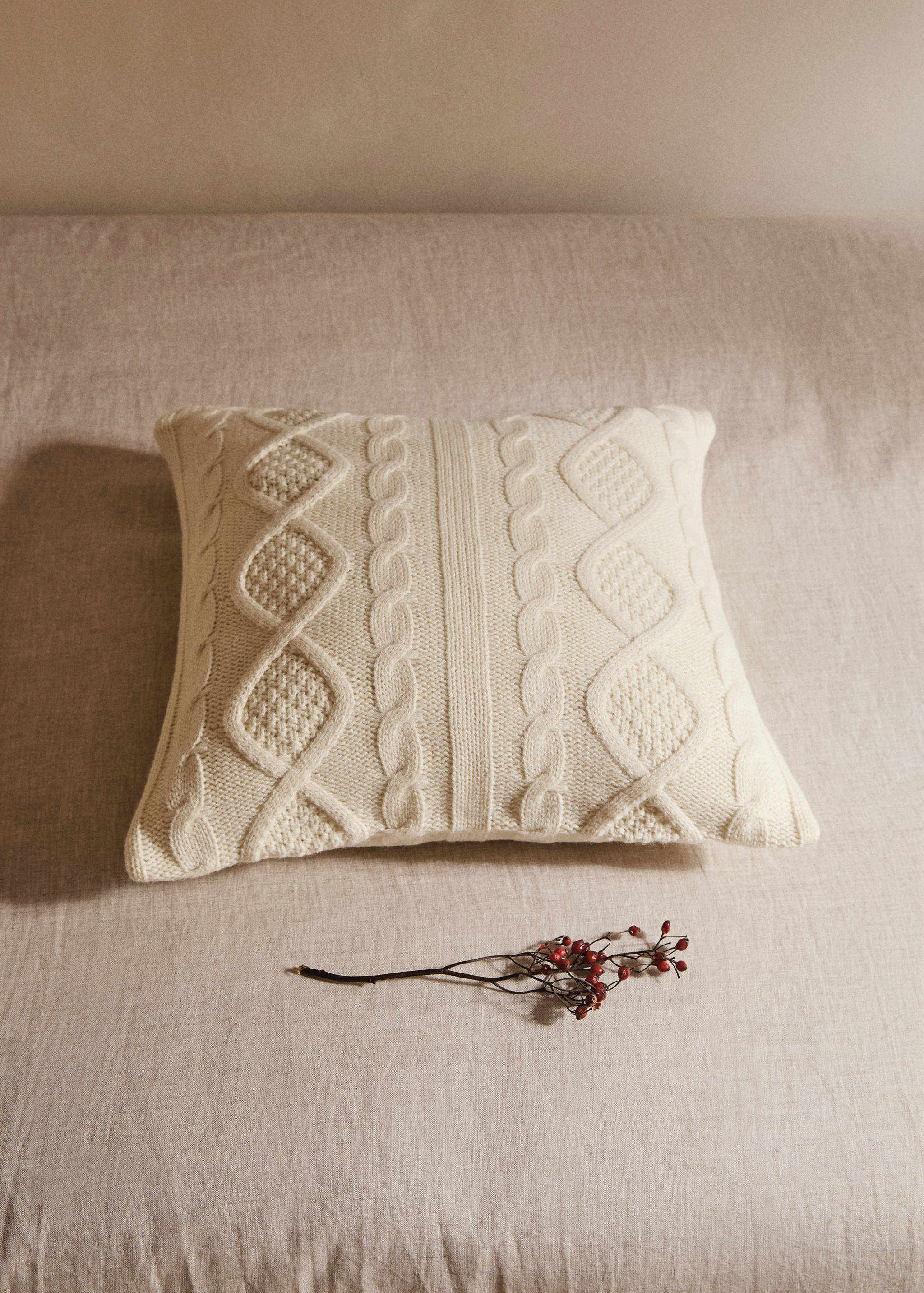 Cream knitted cushion cover with cable and diamond pattern.