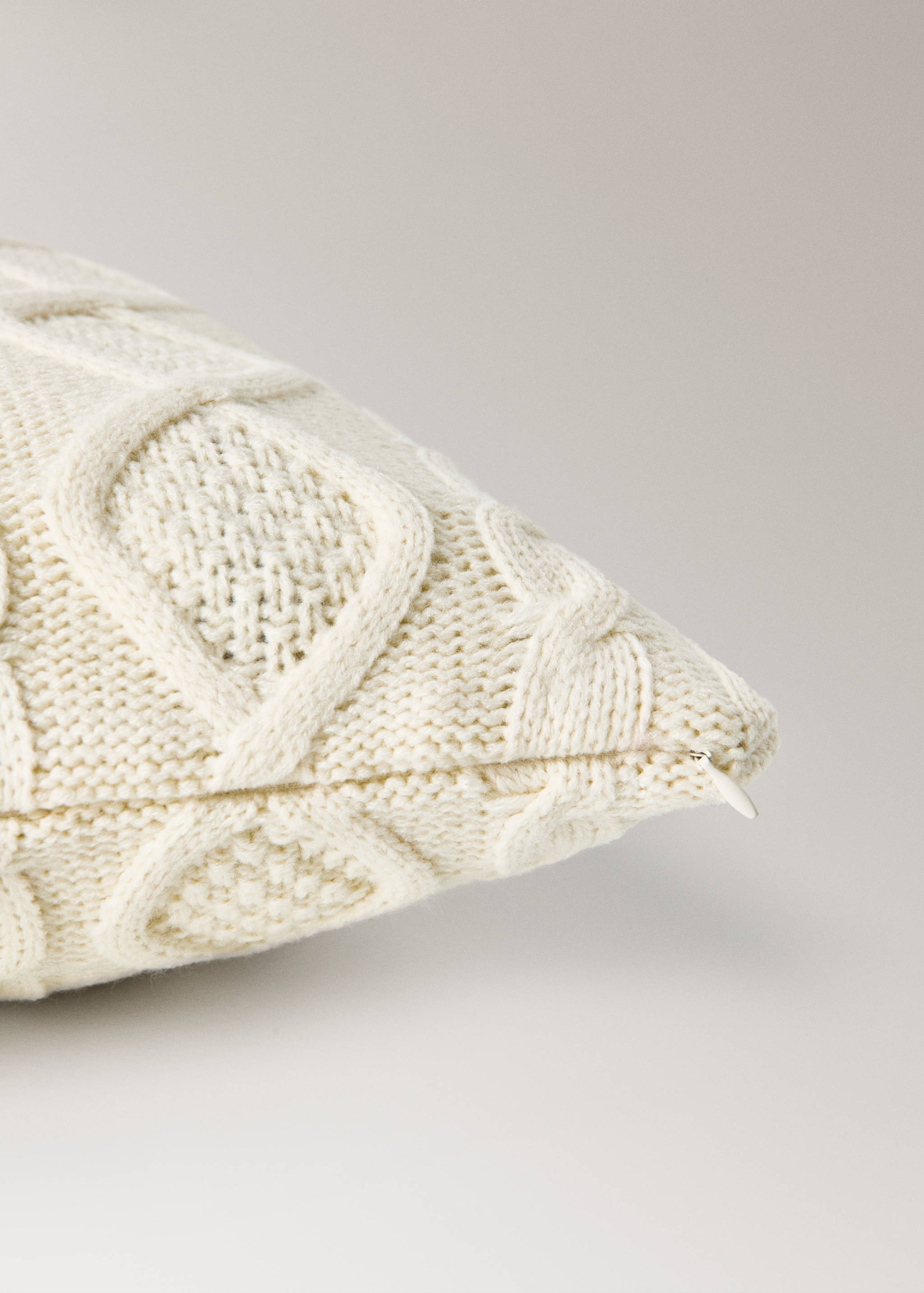 Off-white cable-knit cushion cover detail showing texture and zipper.