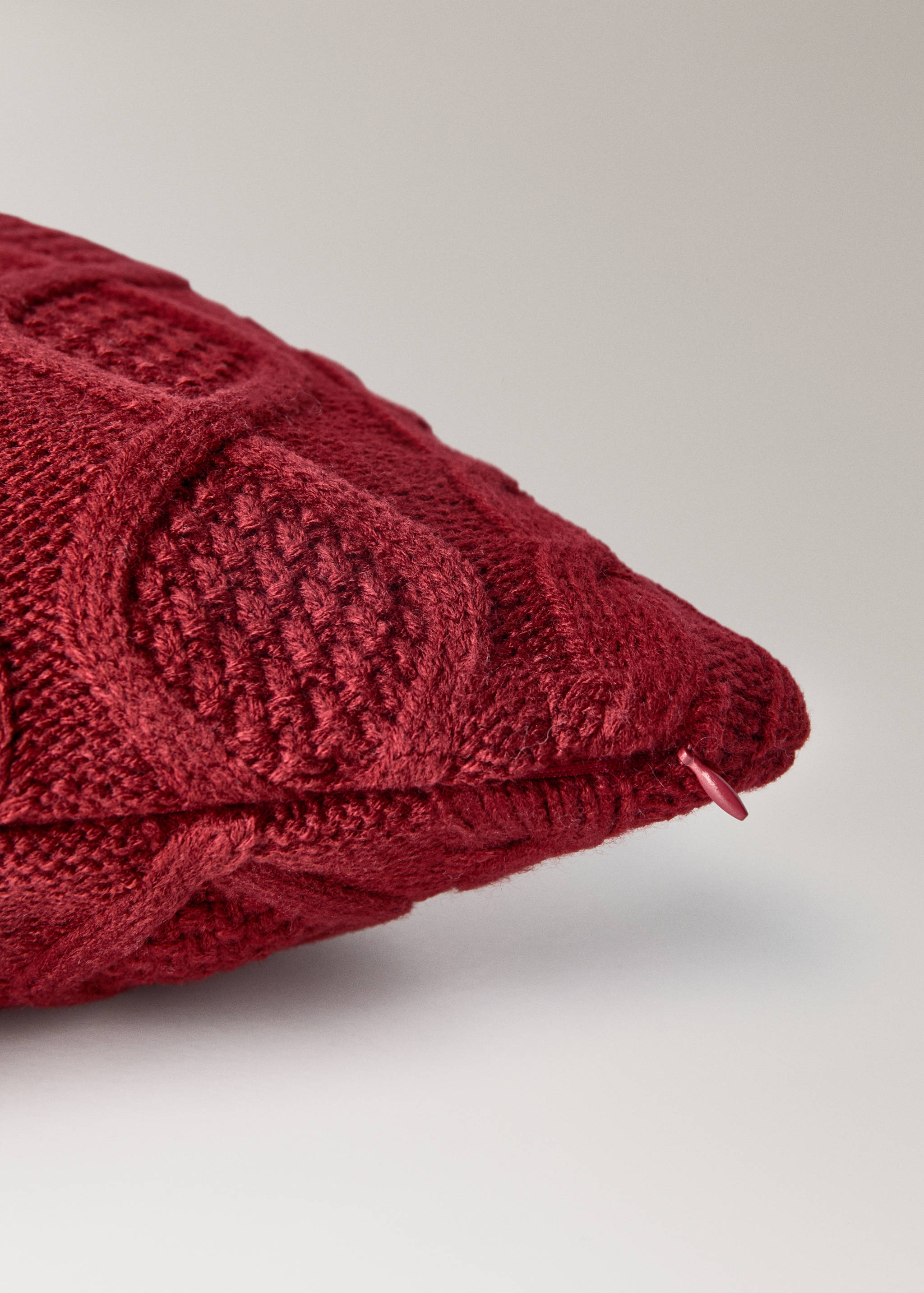 Dark red knitted cushion cover close-up showing texture and zip.