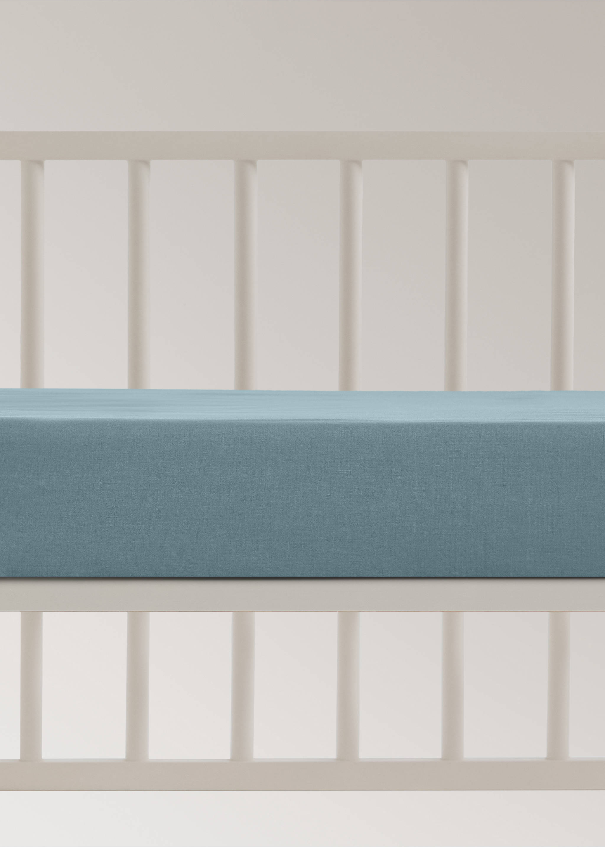 Blue fitted cot sheet on a mattress in a white wooden cot., Blue. Ref: 17071545-00.
