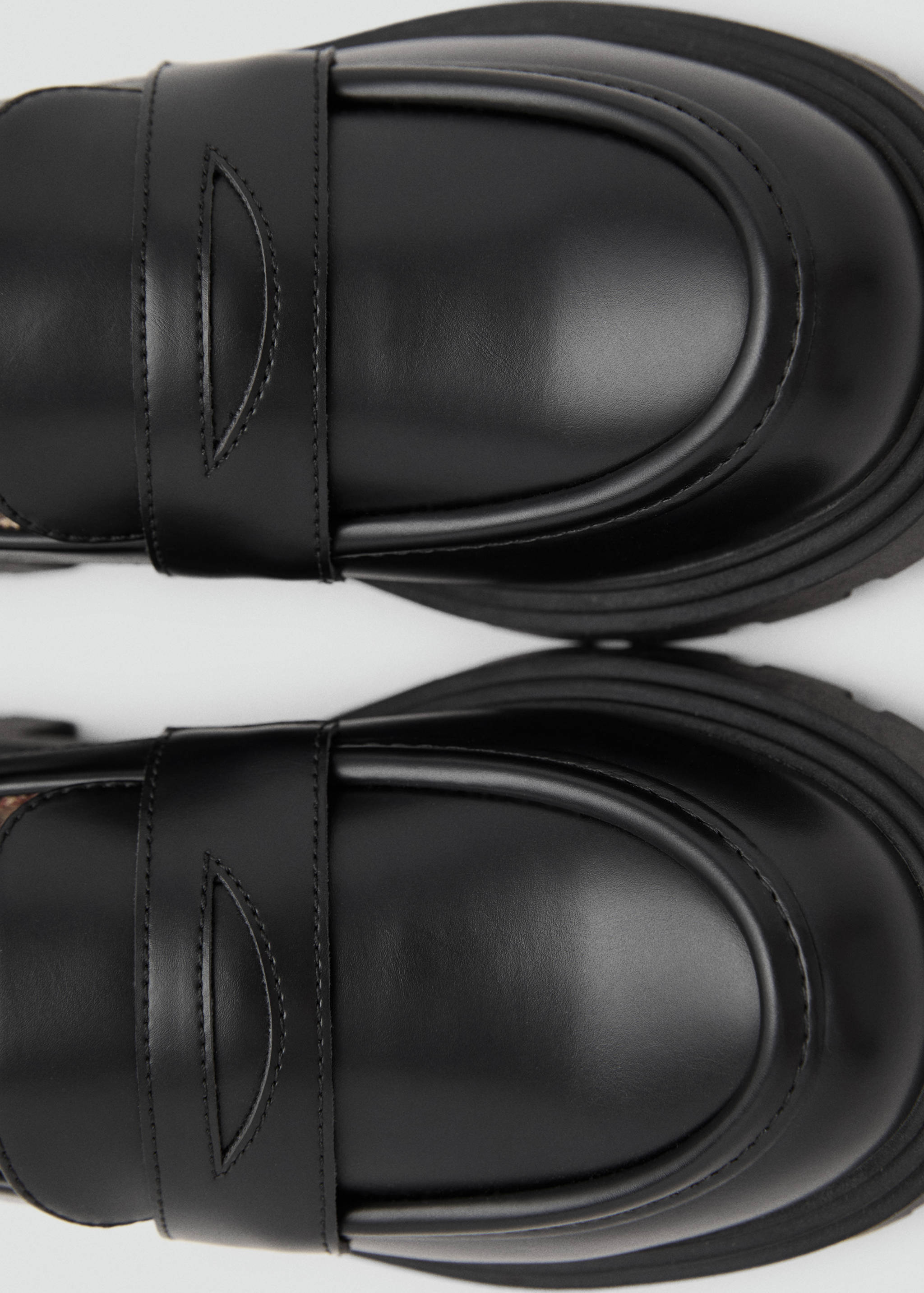 Close-up of black leather-effect penny loafers showing toes and instep strap.