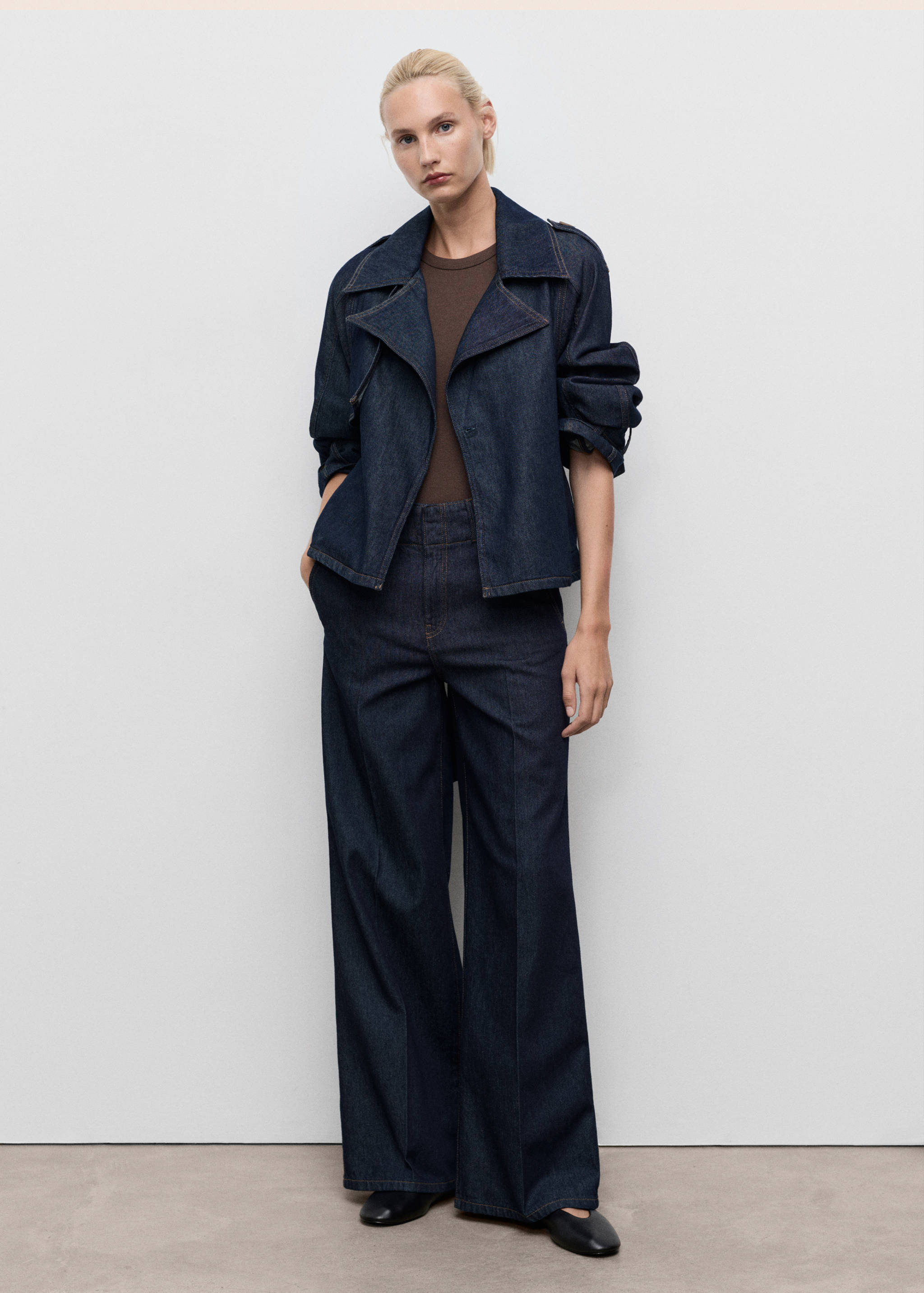 Chaqueta gabardina de denim azul oscuro con solapas anchas, combinada con pantalones fluidos de pernera ancha a juego.