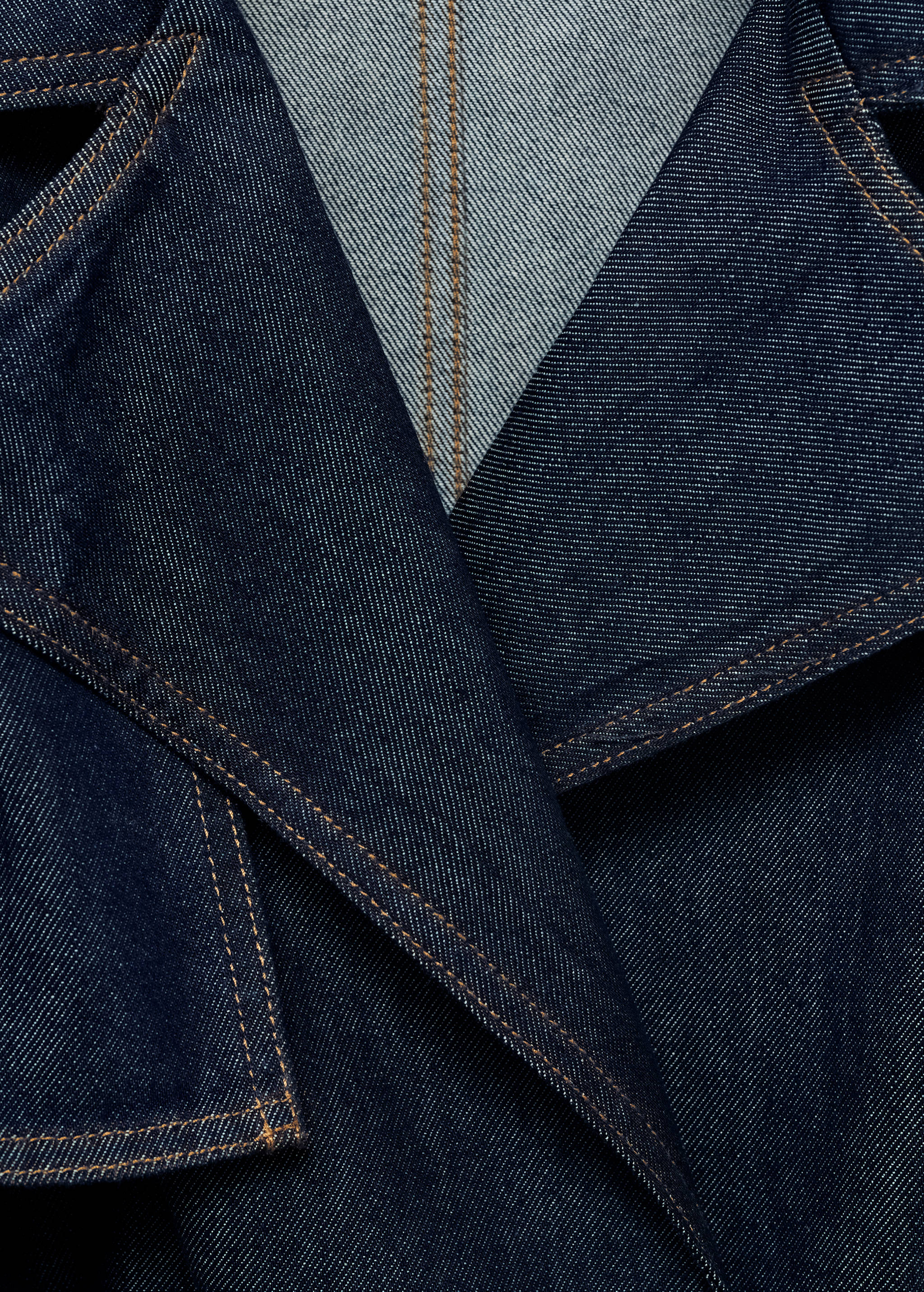 Detalle de gabardina vaquera en azul oscuro con costuras en contraste.
