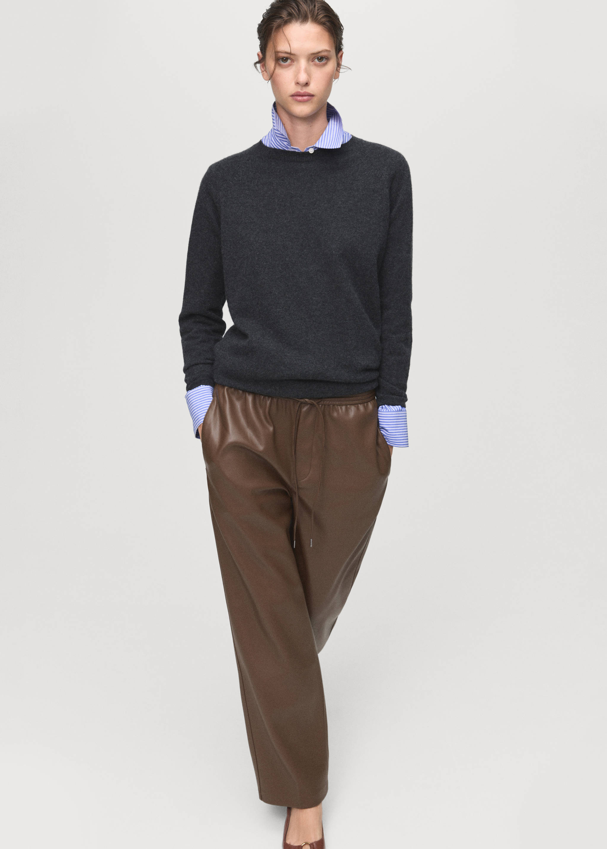 Brown faux-leather trousers with a drawstring waist, styled with a grey jumper and striped shirt.