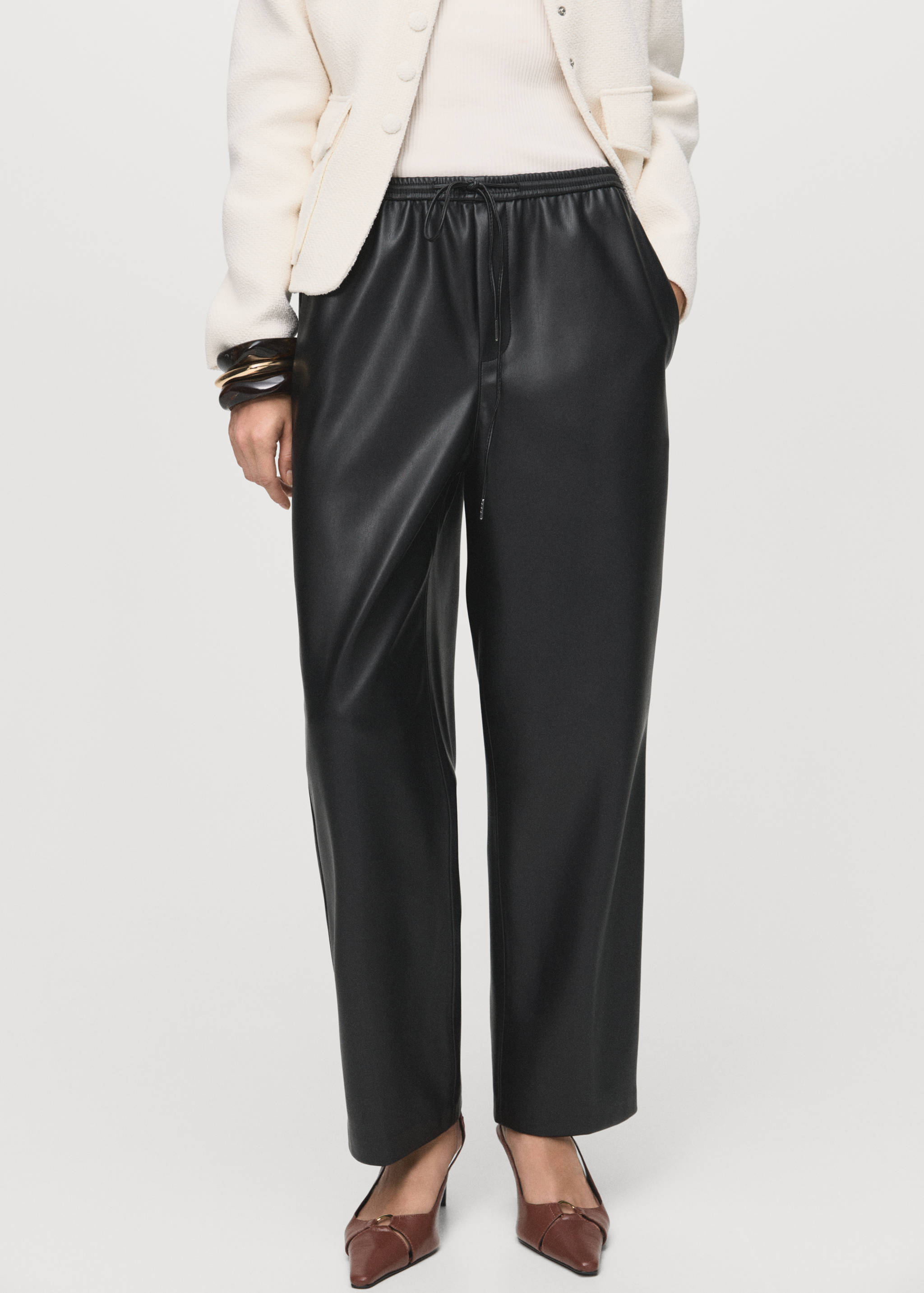 Black faux-leather trousers with a drawstring waist, worn with a cream jacket.