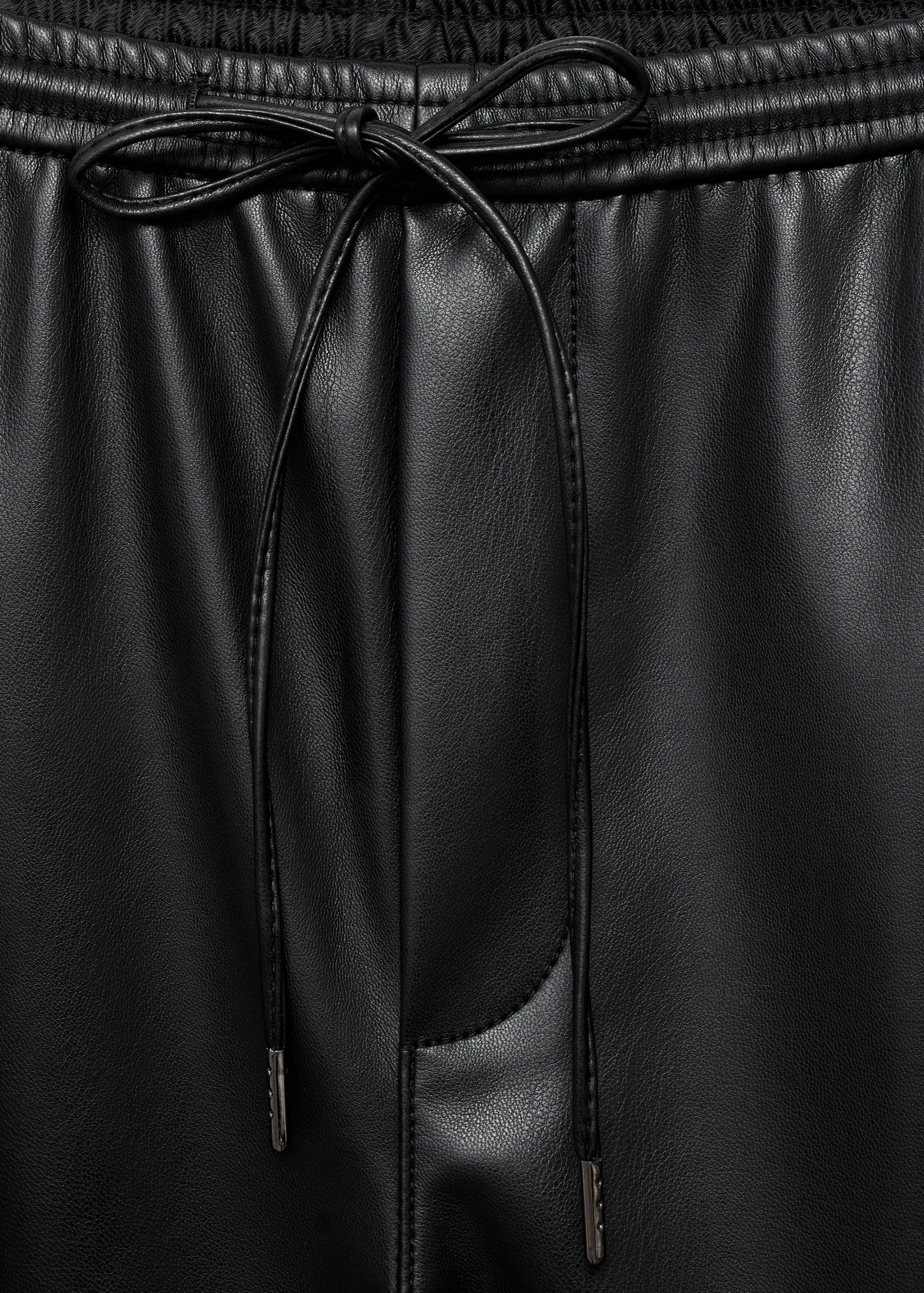 Close-up of black faux-leather trousers with an elasticated drawstring waistband.