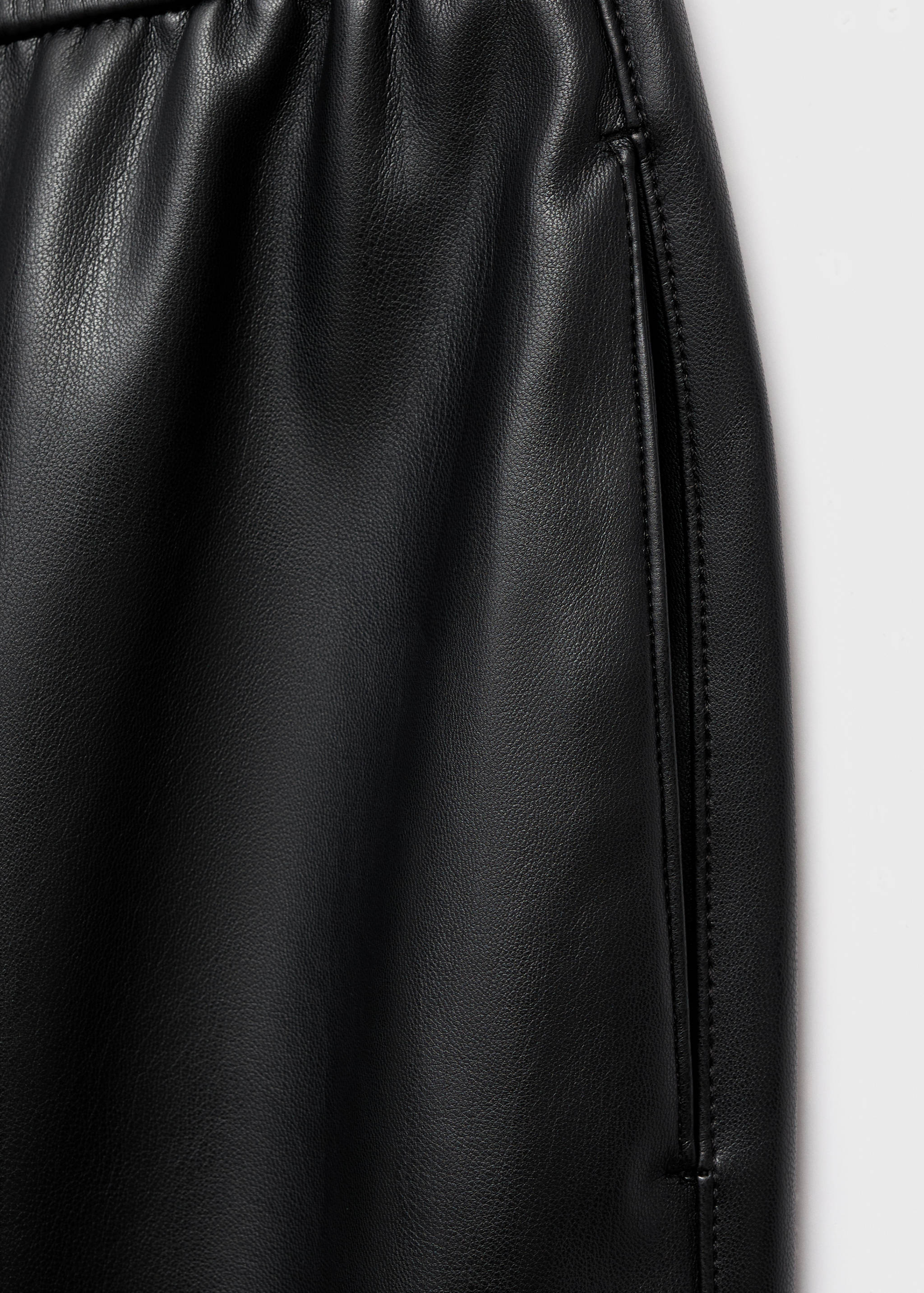 Close-up of black faux-leather trousers highlighting the fabric texture.