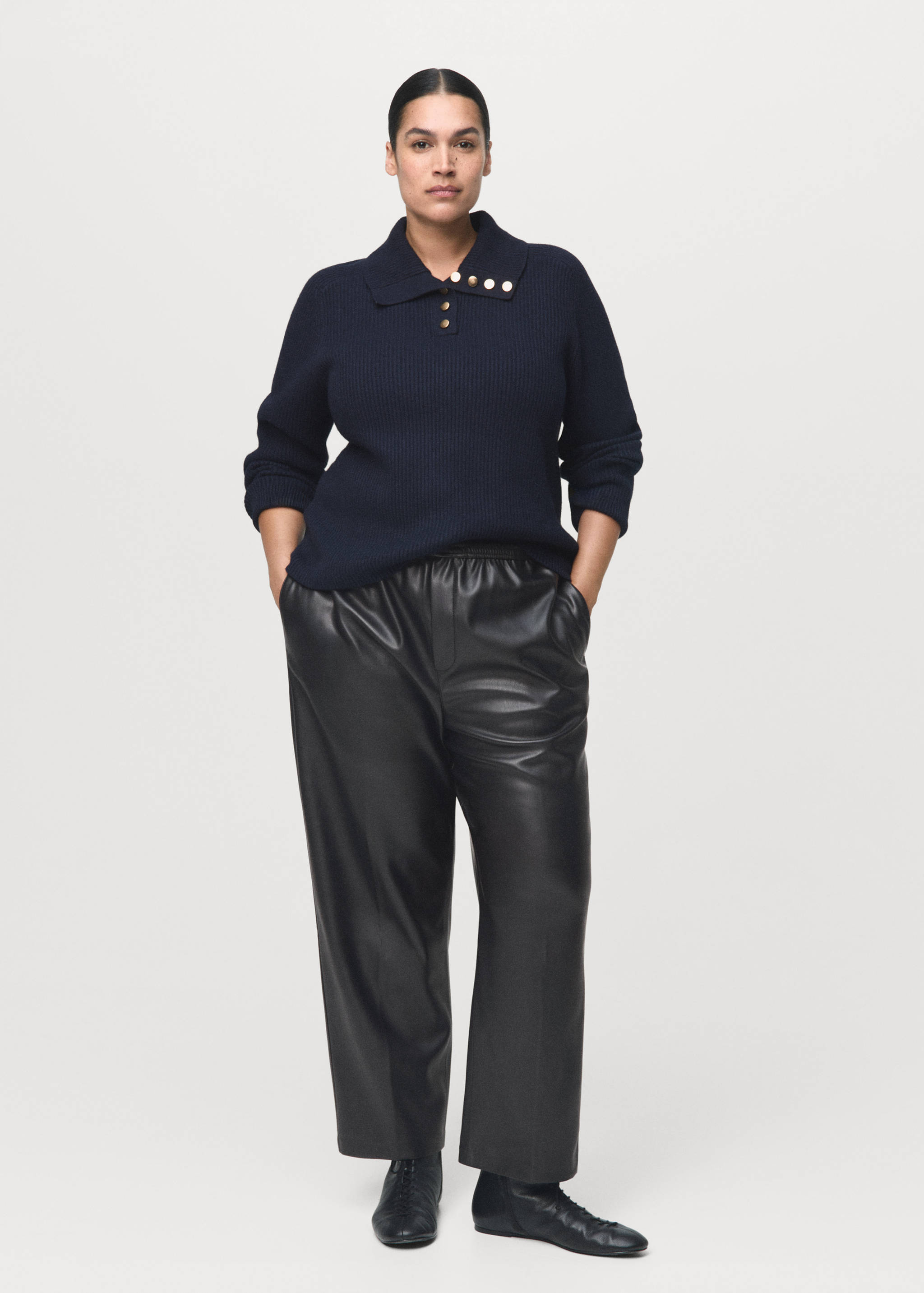 Black faux-leather trousers with a relaxed fit, worn with a dark navy knit polo sweater.