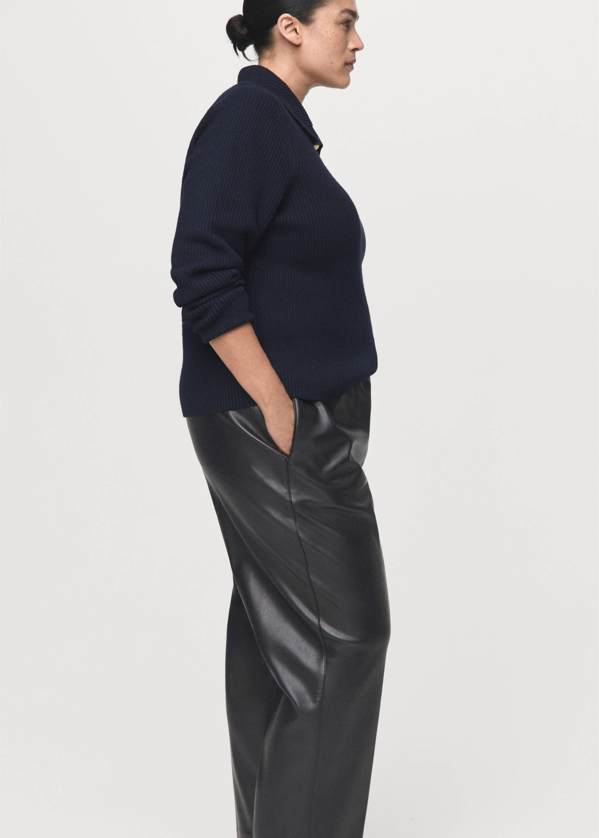 Dark faux-leather trousers with side pockets, worn with a navy blue ribbed jumper.