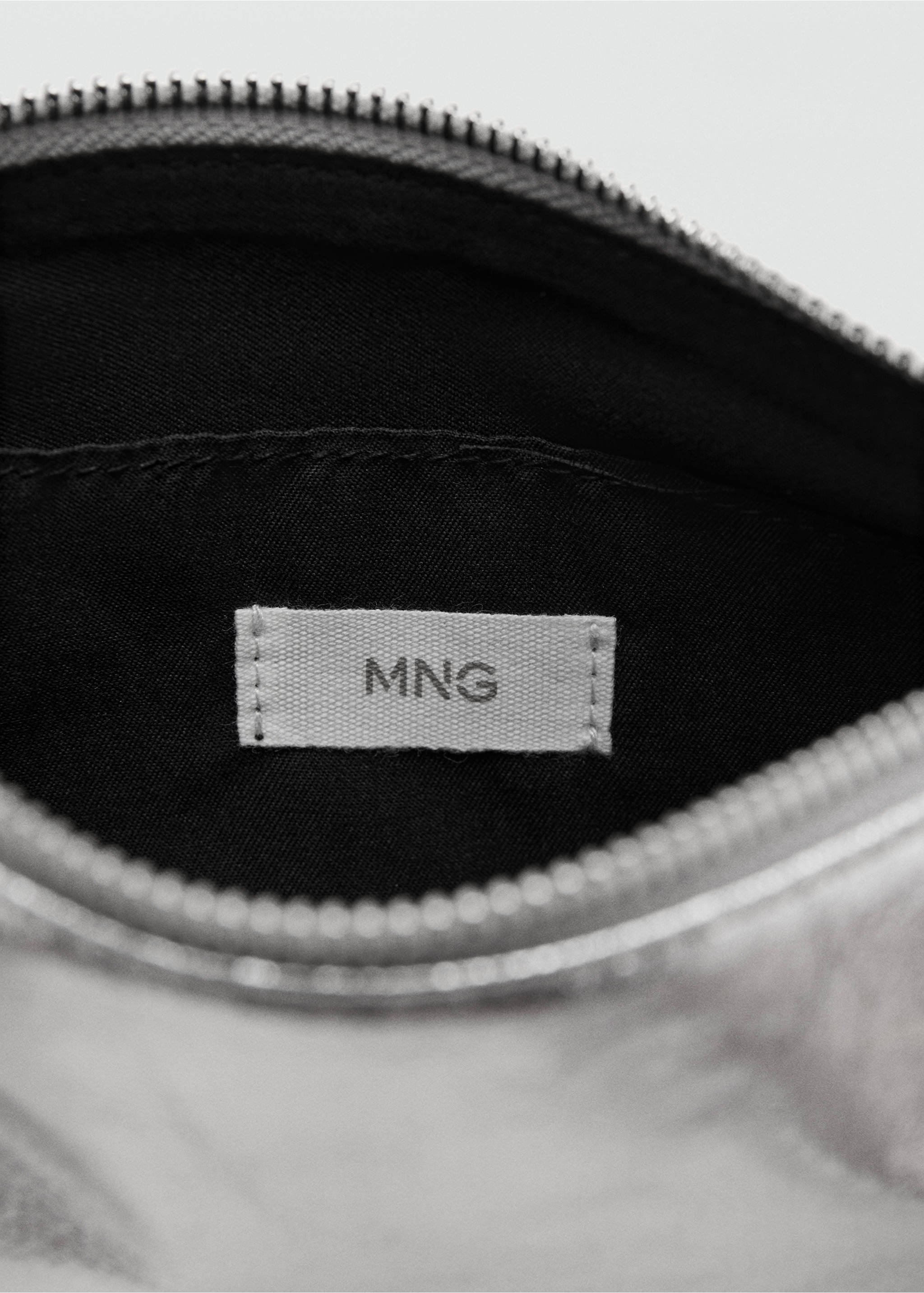 Interior detail of a silver gadget case with a black lining and MNG logo label., Silver. Ref: 17077890-00.