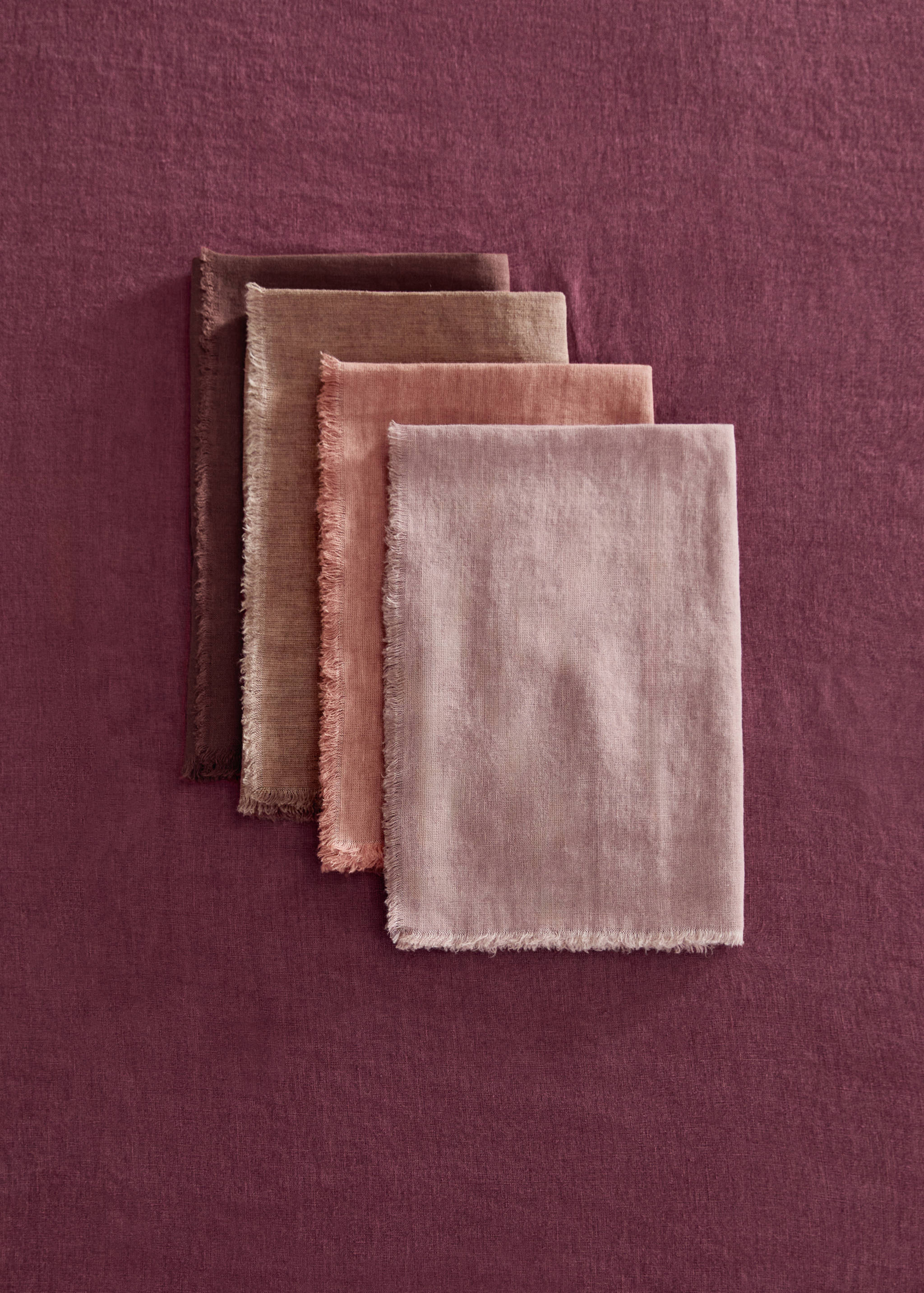 Four fringed fabric napkins in graduated shades of pink, mauve, and brown.