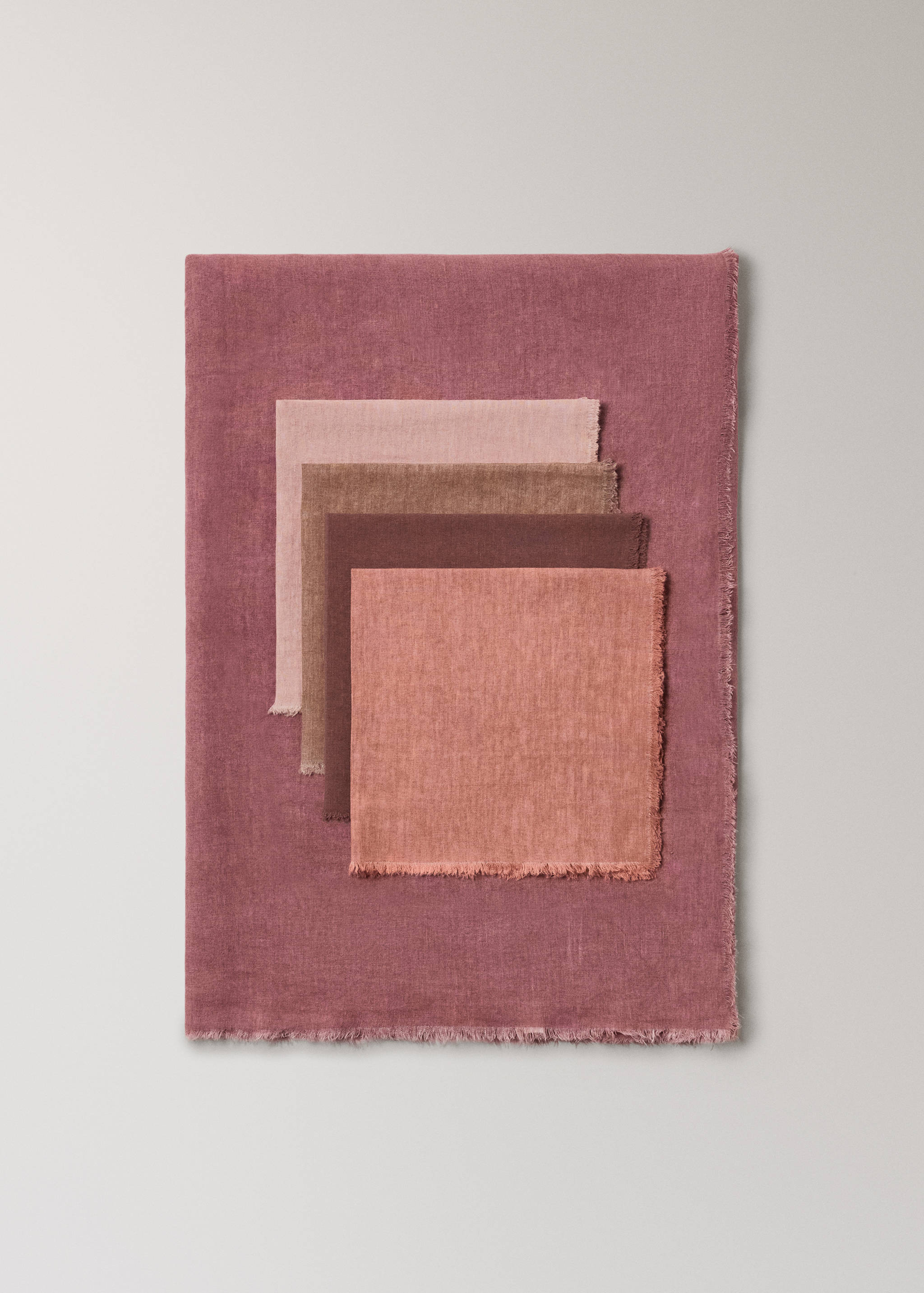 Close-up of five layered fabric napkins in dusty rose, pink, brown, terracotta and coral with frayed edges.