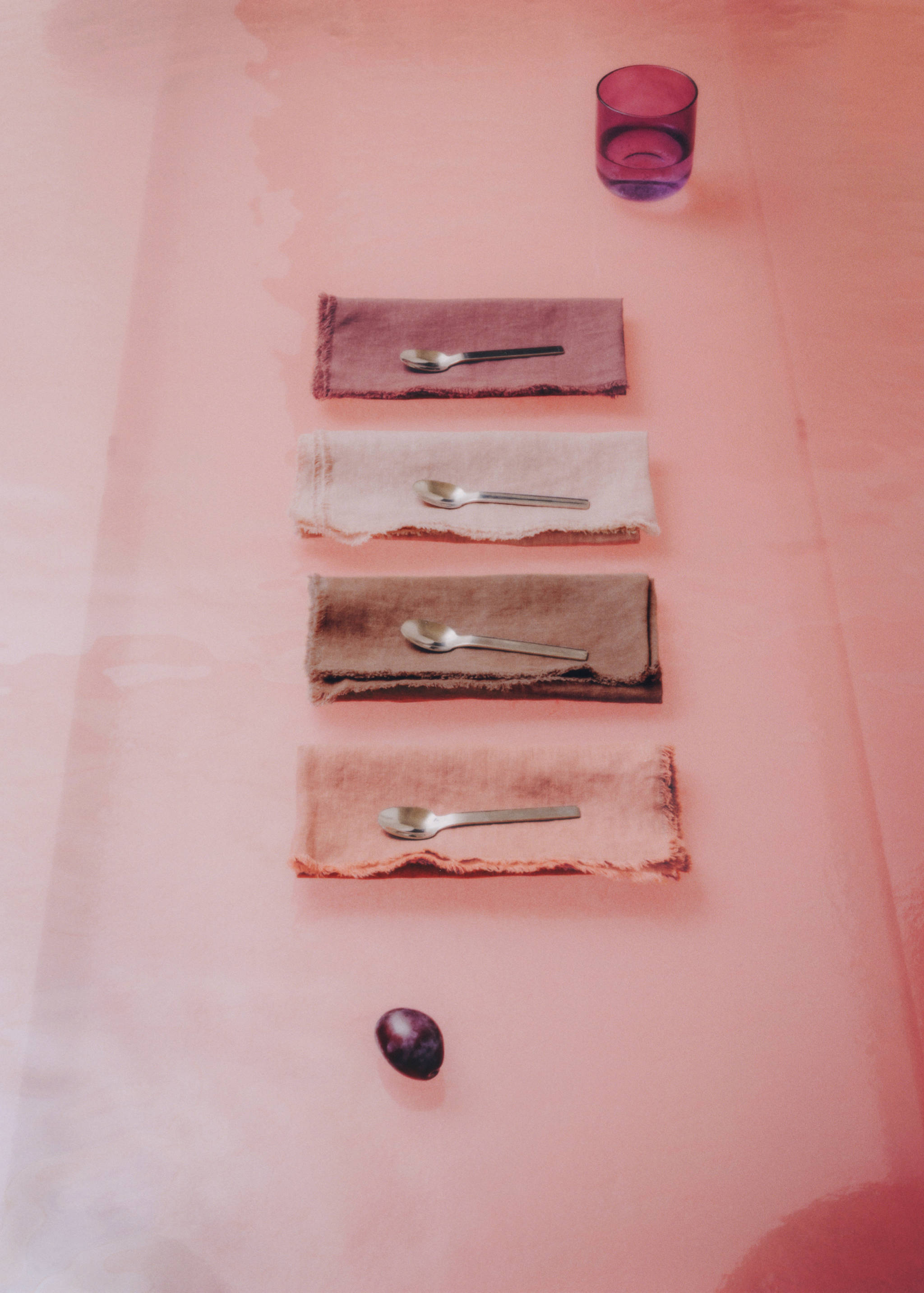 Four frayed cloth napkins in various earthy tones, stacked on a pink tabletop.