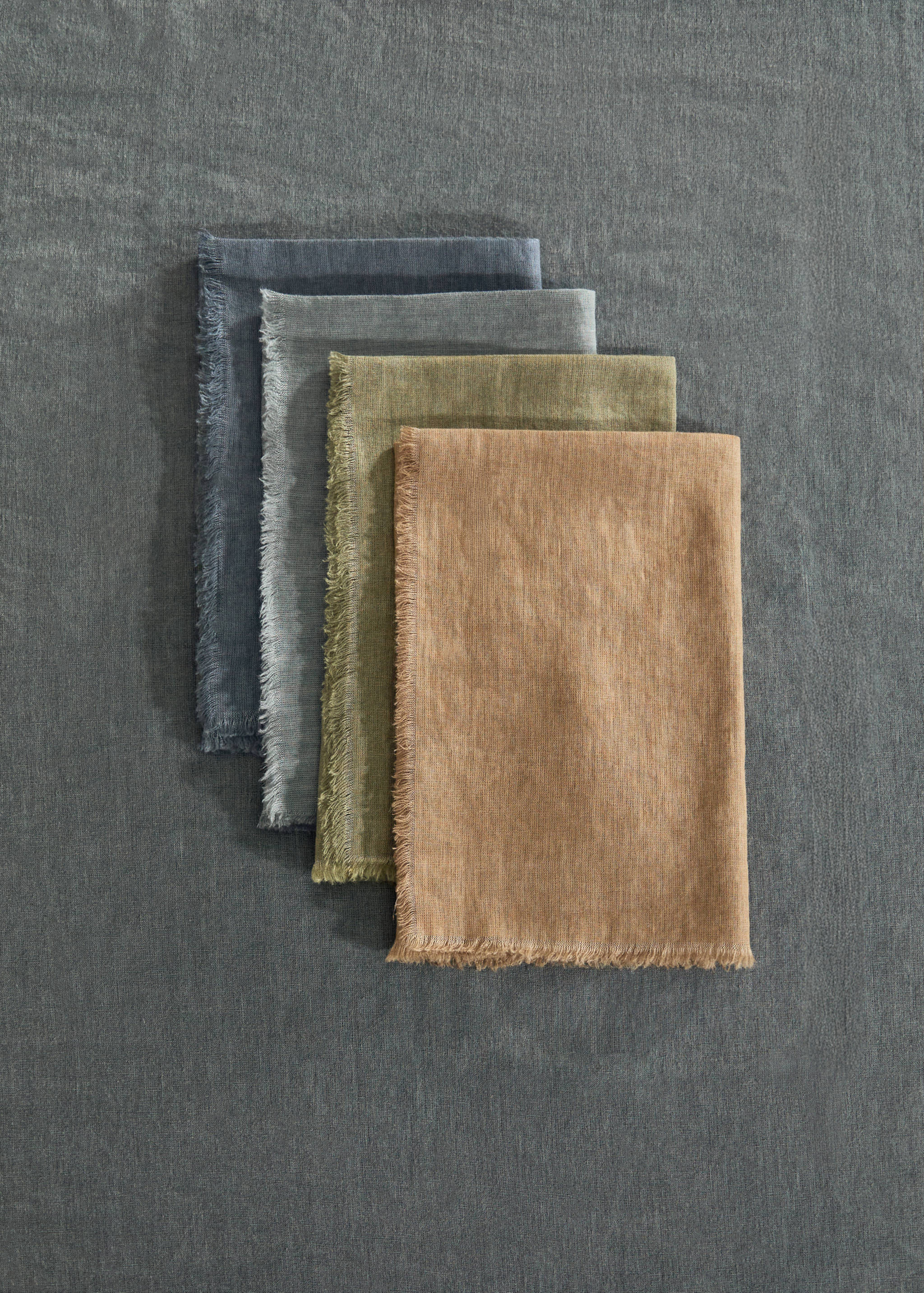 Four folded fringed napkins stacked in blue, grey, olive, and ochre.