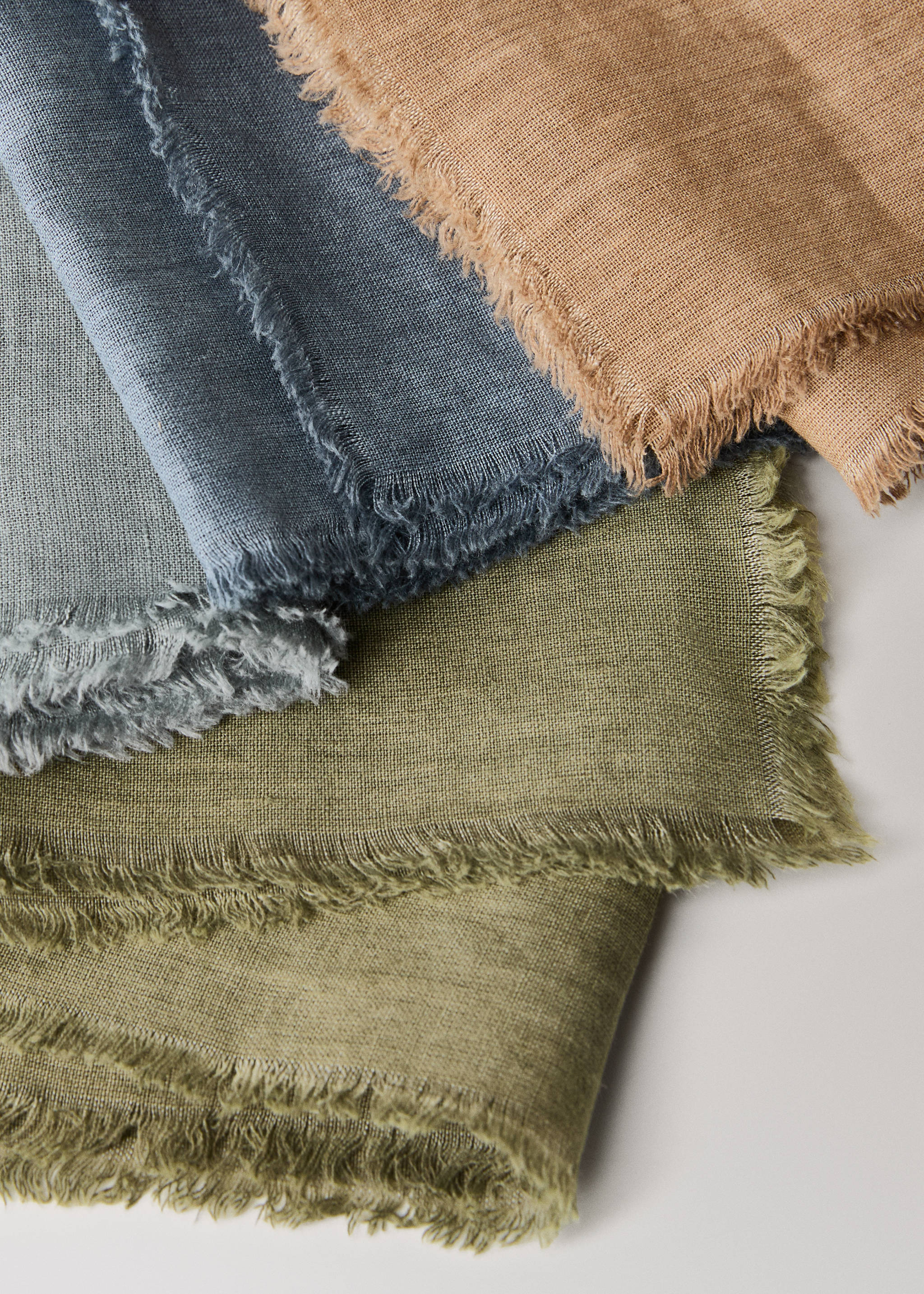 Close-up of fringed fabric napkins in camel, grey-blue, and olive green.