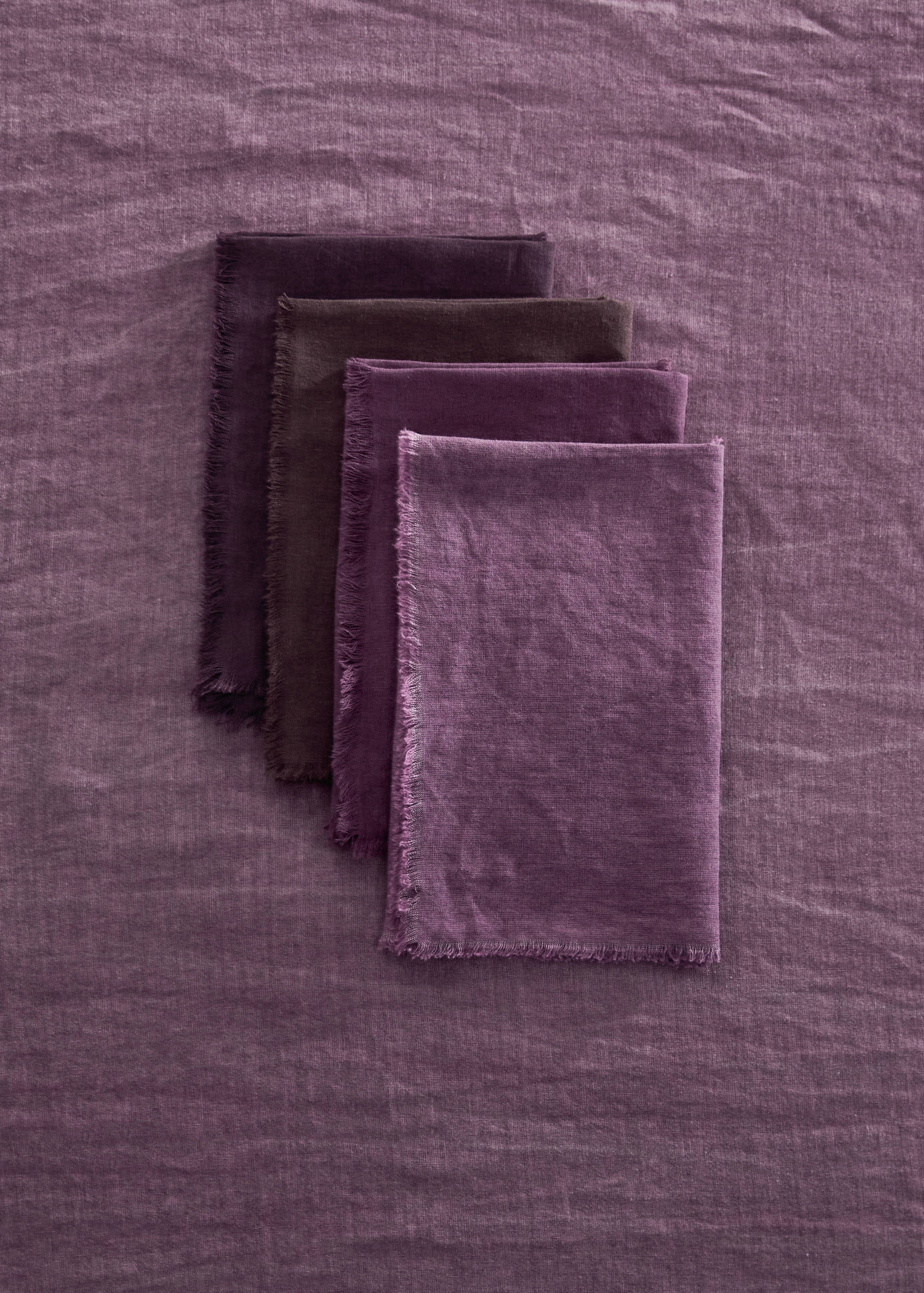 Set of four purple napkins with frayed edges, stacked diagonally.