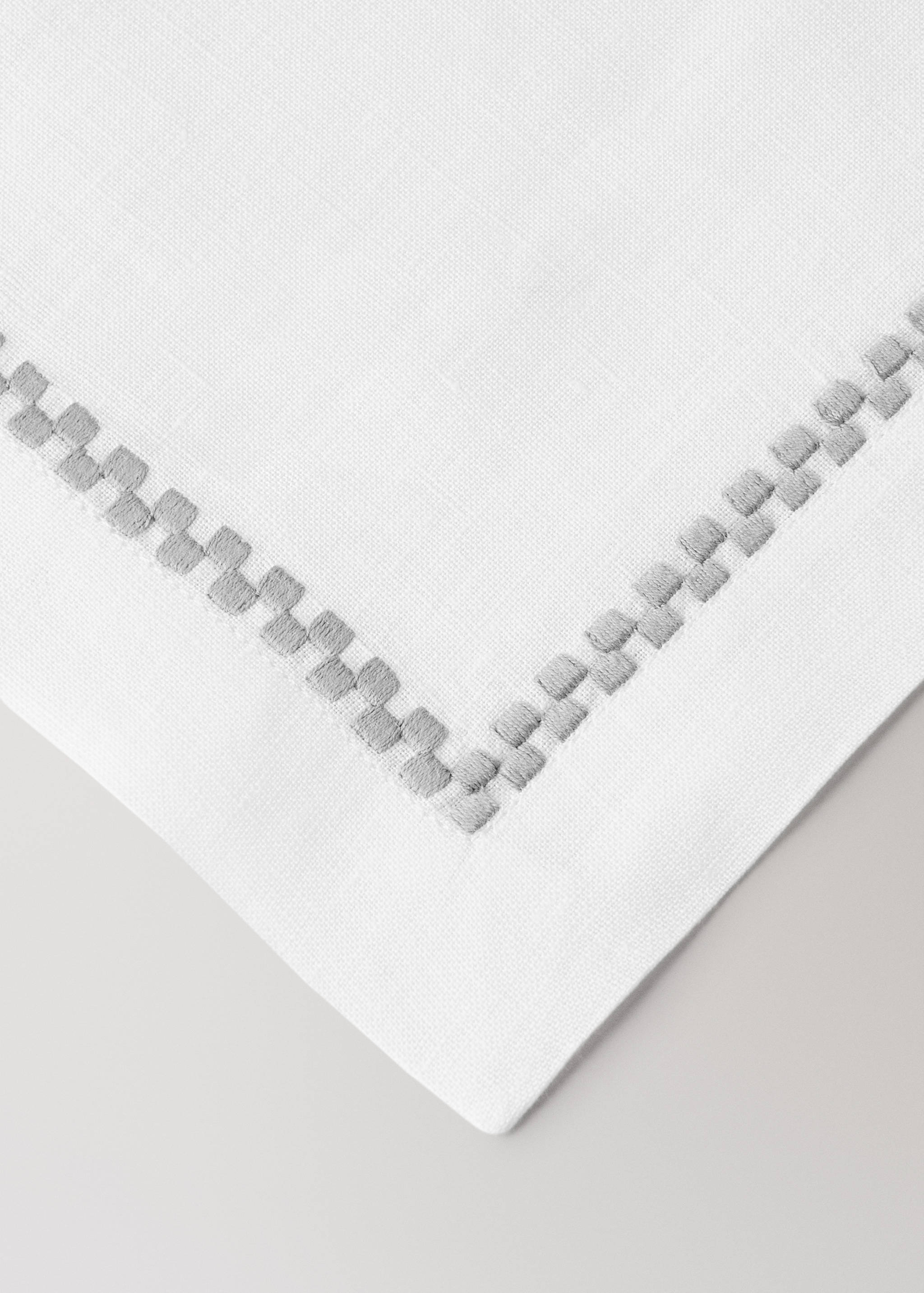 White placemat with grey embroidered geometric border detail.