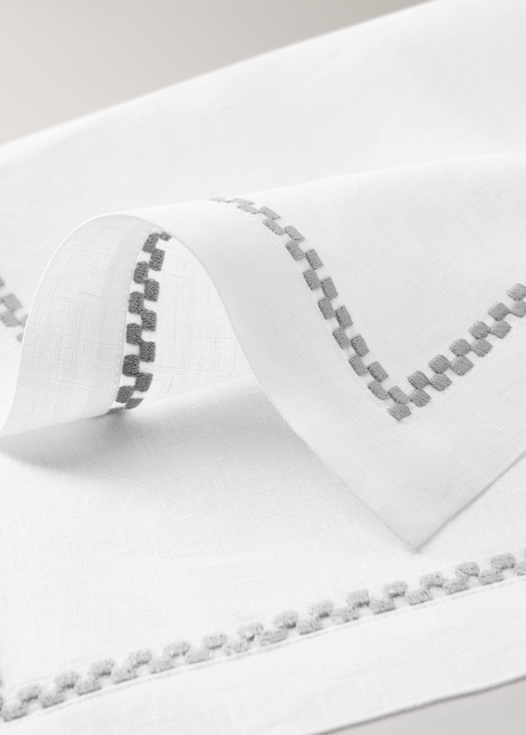White placemat detail with a grey embroidered geometric border.