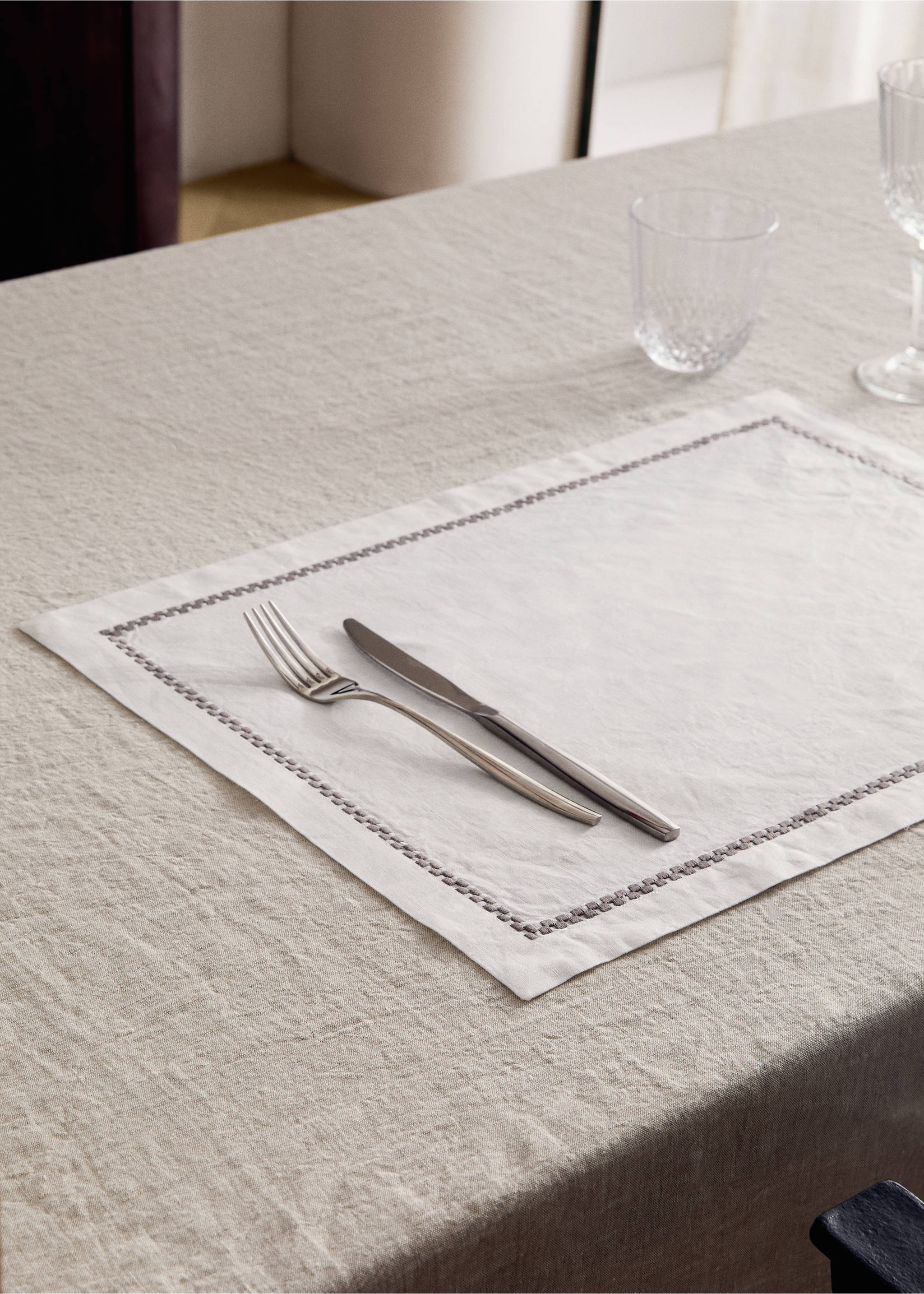 Off-white placemat with a dark stitched border, set on a dining table., Light/Pastel Brown. Ref: 17083826-00.