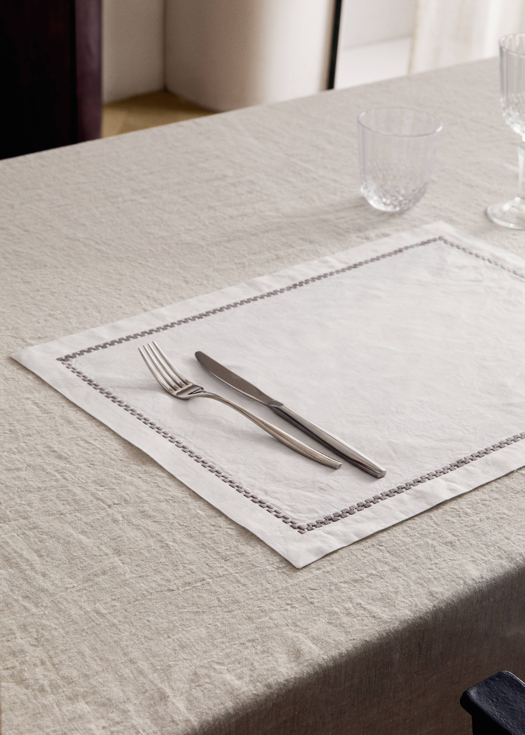 Off-white placemat with a dark stitched border, set on a dining table.