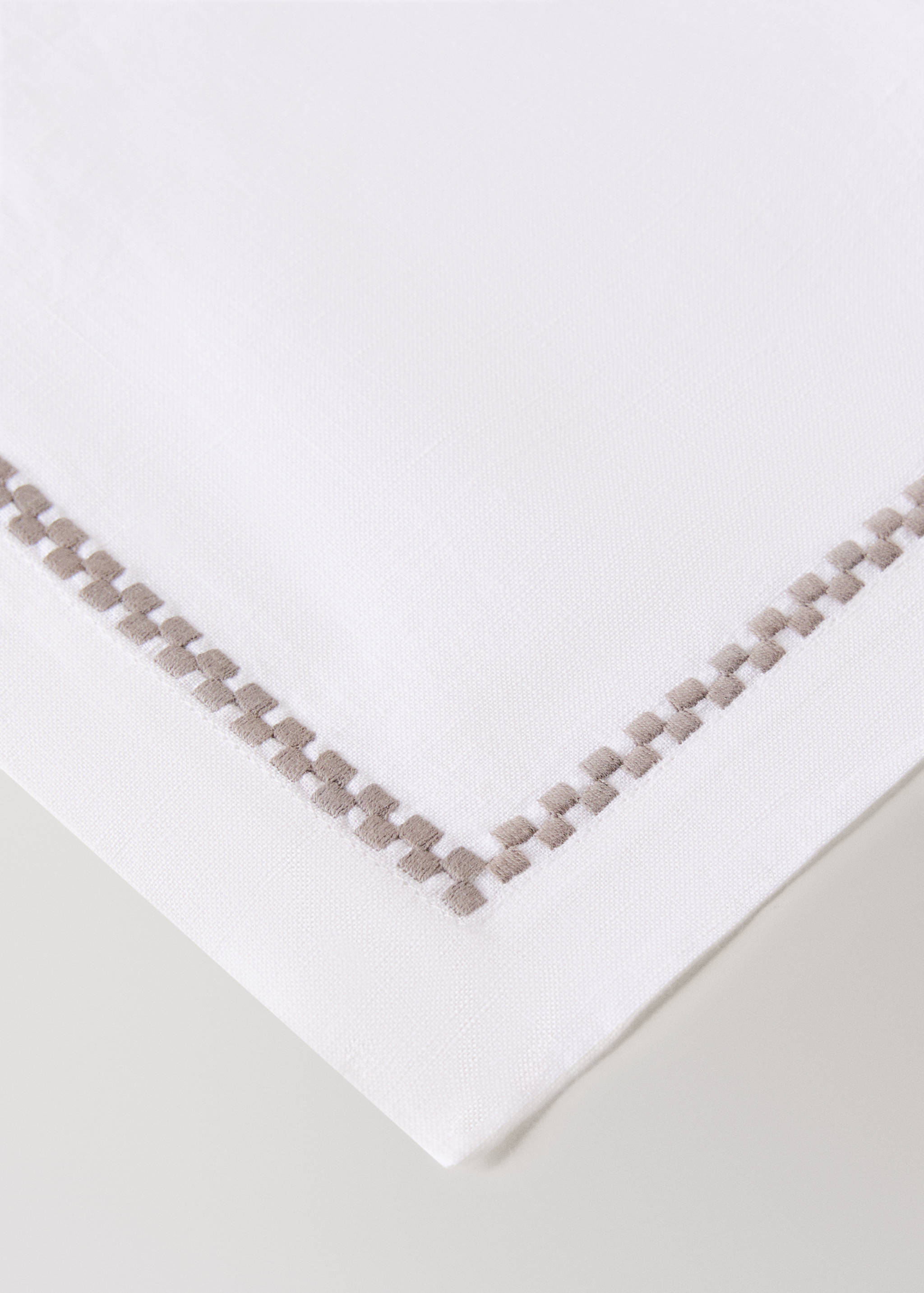 White placemat with an embroidered light grey-brown geometric border.
