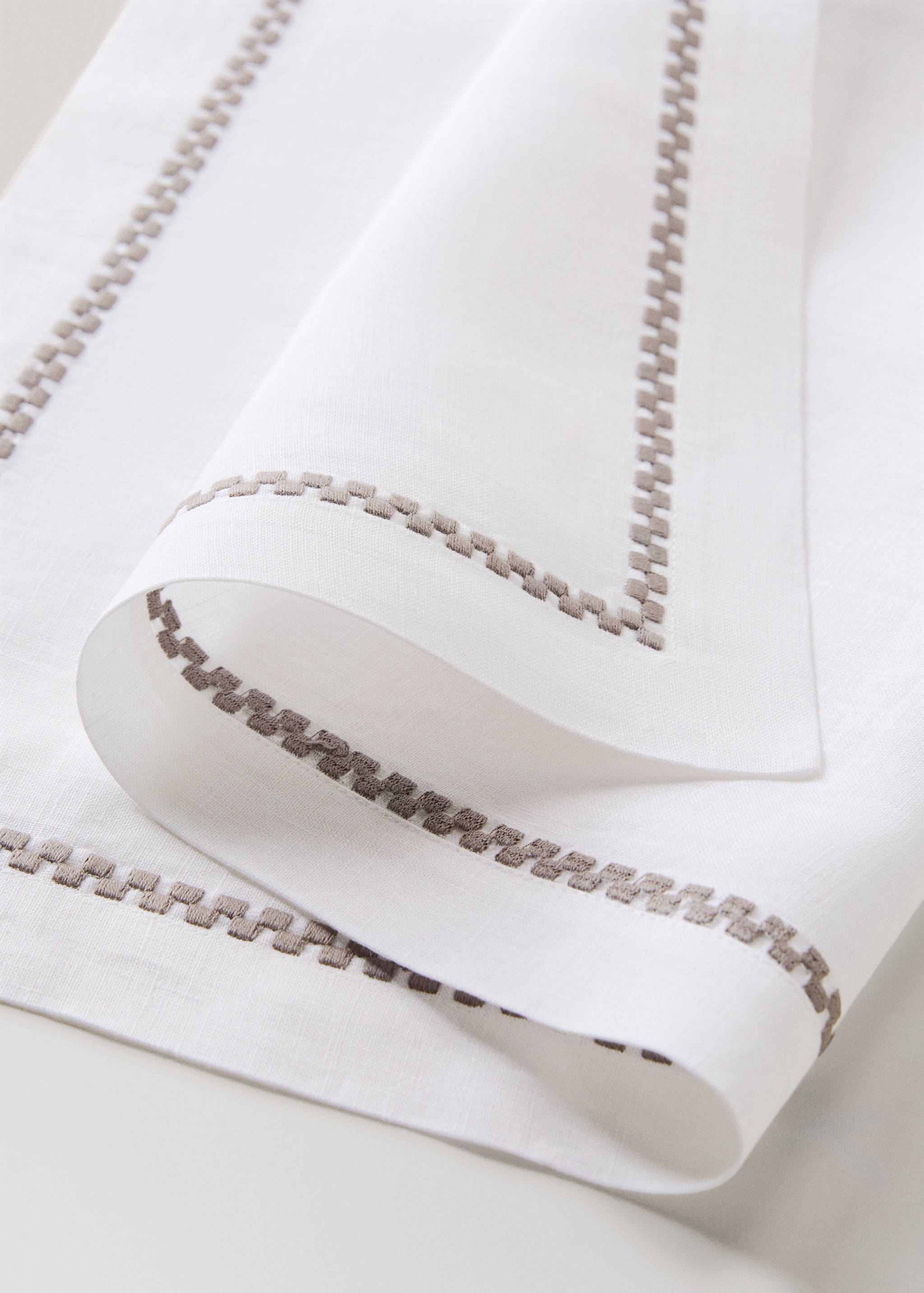 White individual placemat with a beige embroidered geometric border.