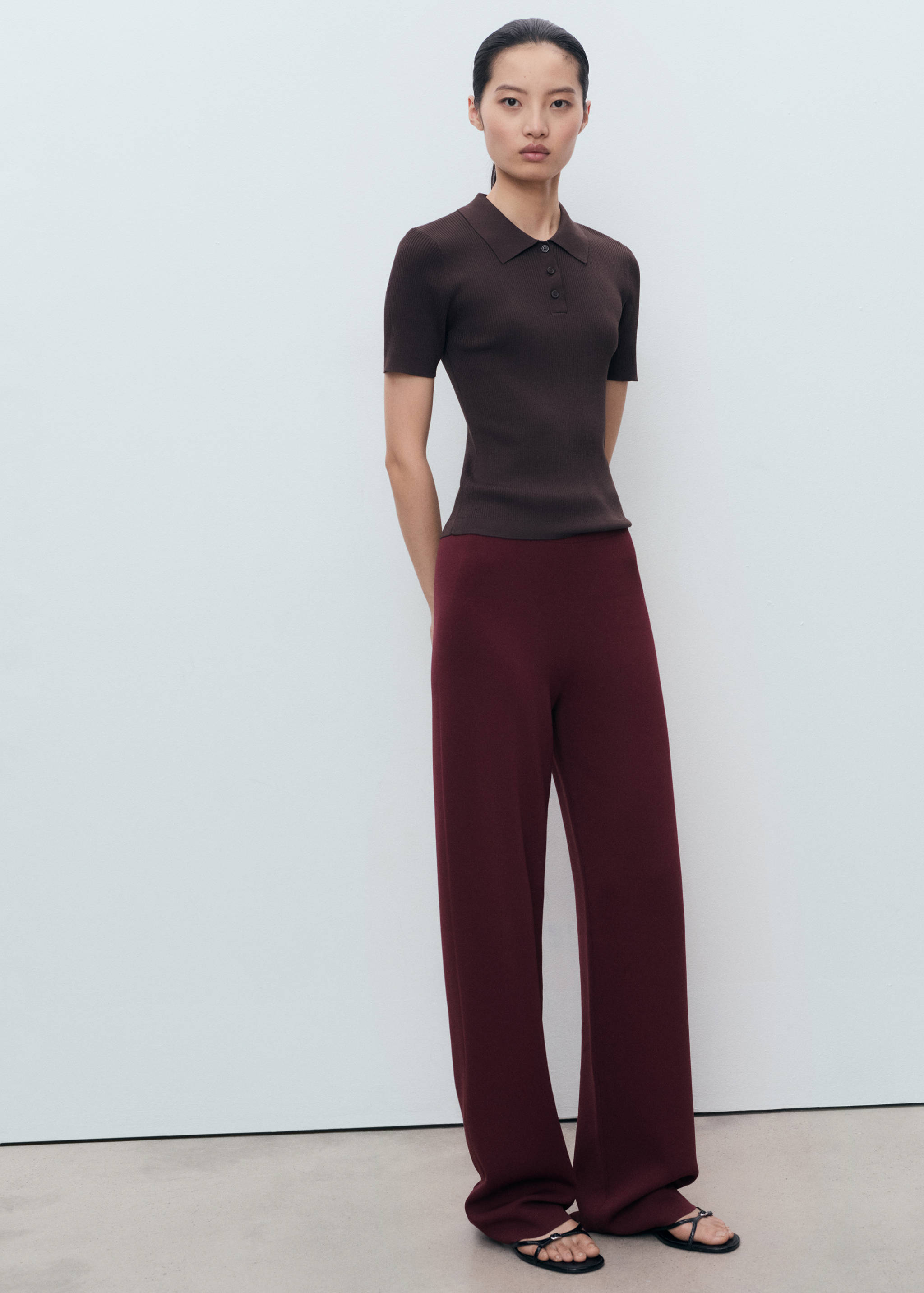 Pantalones burdeos de corte ancho combinados con un polo de punto marrón oscuro de manga corta.