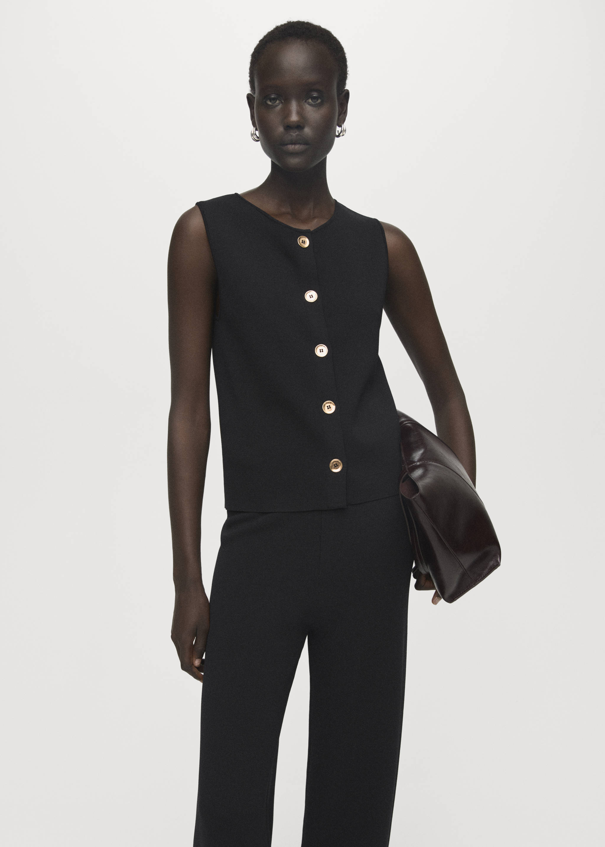 Pantalones negros combinados en conjunto con un top sin mangas con botones delanteros.