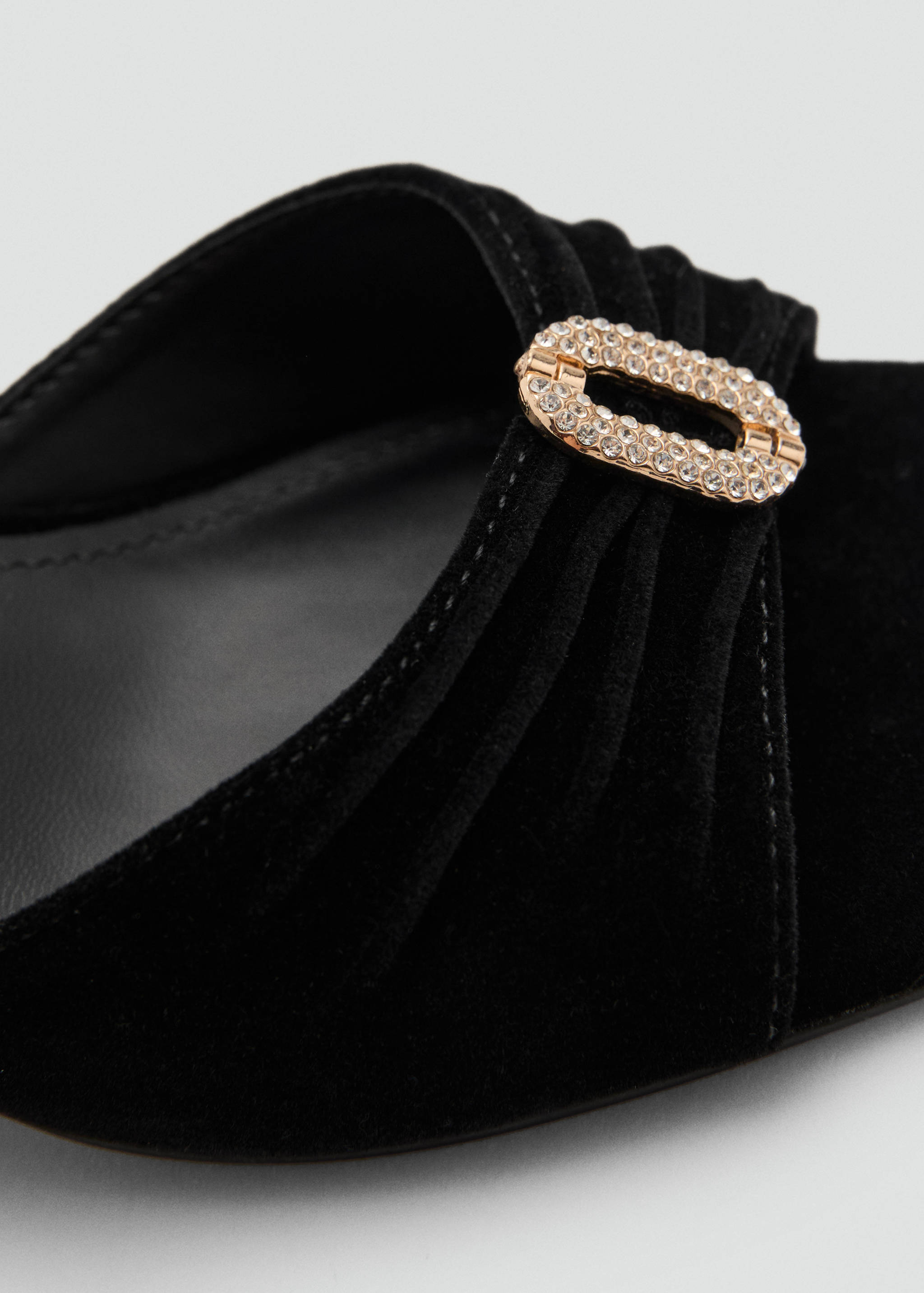 Close-up of black shoe with ruched detail and crystal buckle.