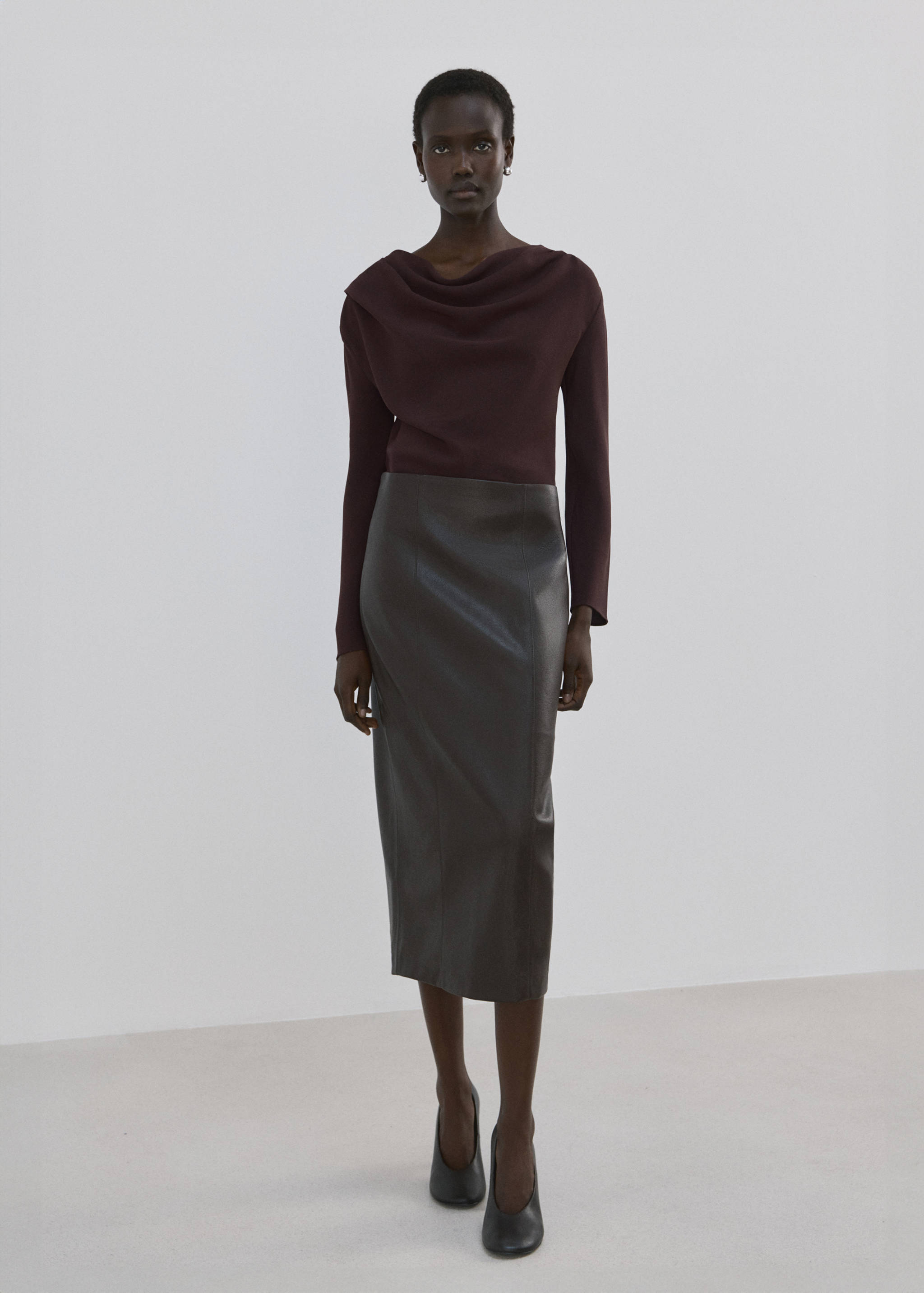 Dark burgundy blouse with a draped cowl neckline and long sleeves, worn with a dark midi skirt.