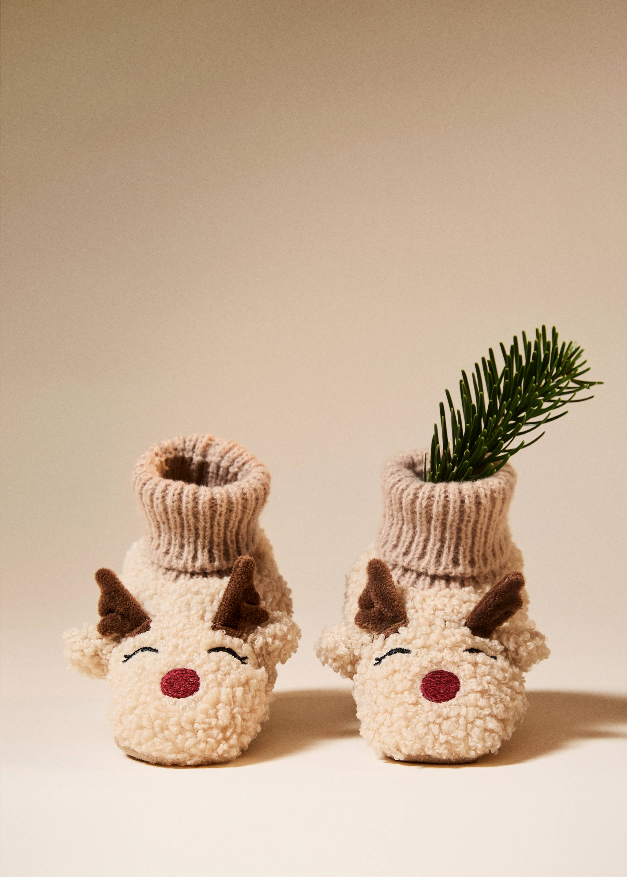 Beige faux-fur house slippers with ribbed cuffs and embroidered reindeer face details.