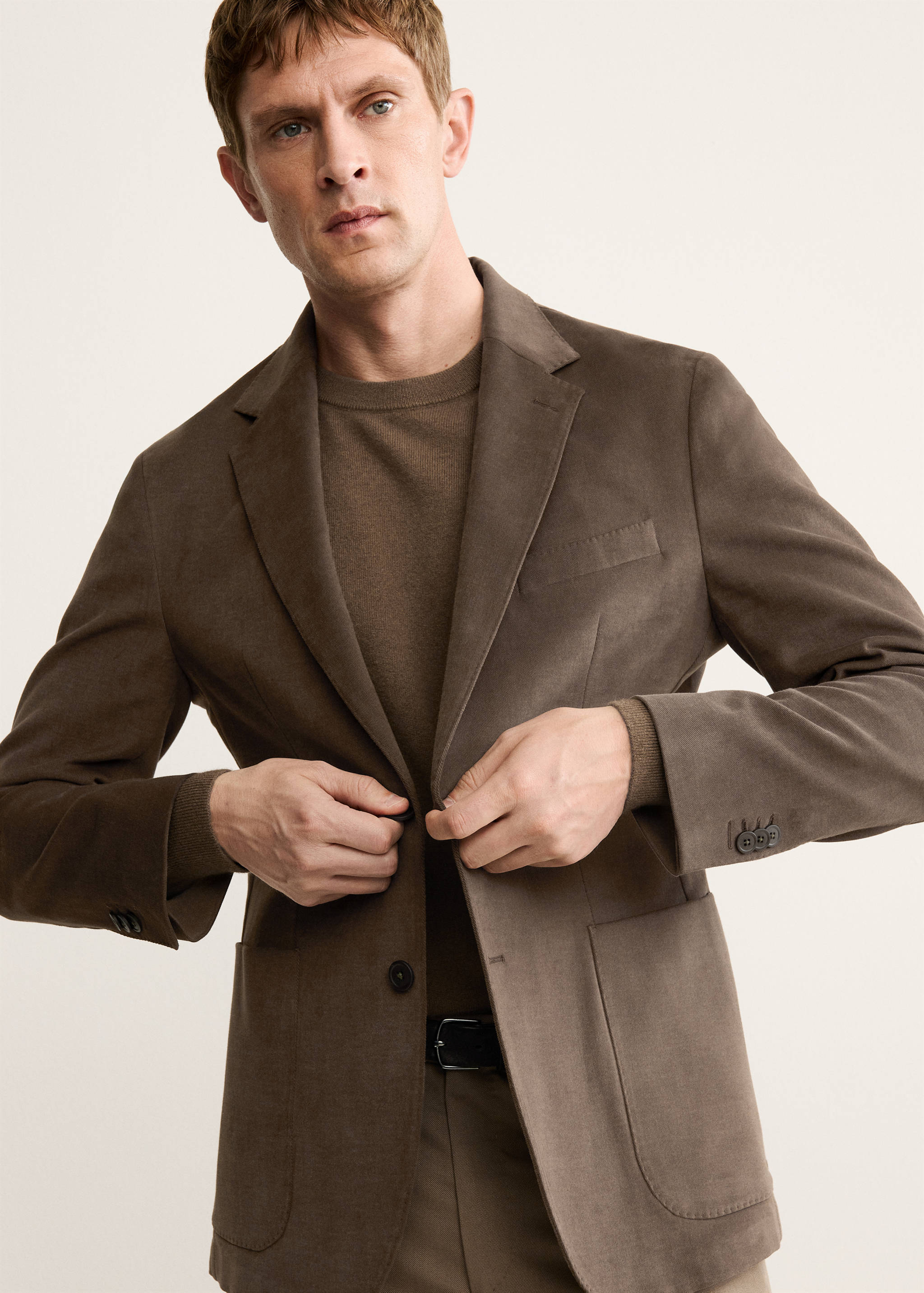 Brown blazer with notched lapels and patch pockets, worn with a brown crew-neck jumper.