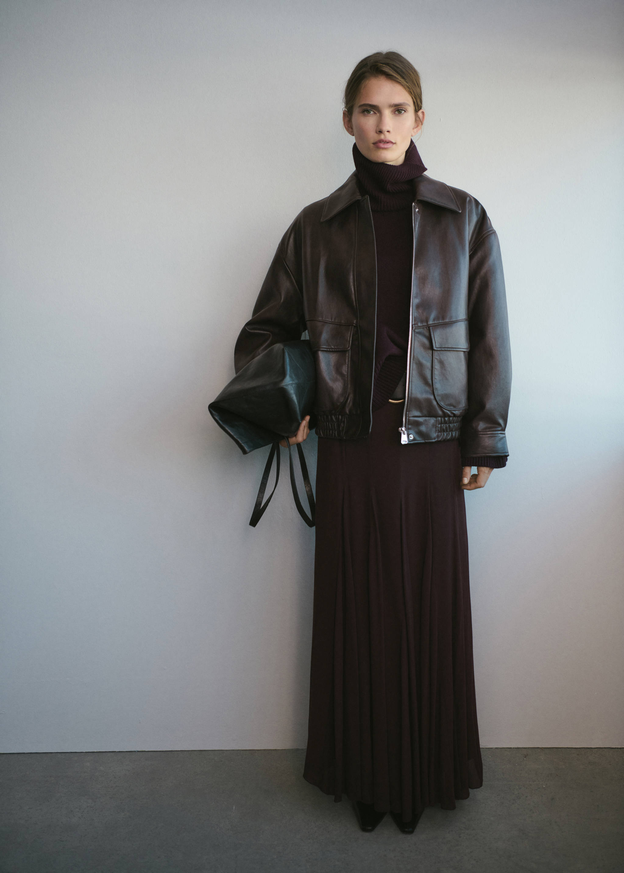 Dark brown leather jacket with collar, zip fastening, and flap pockets, worn with a burgundy sweater and skirt.